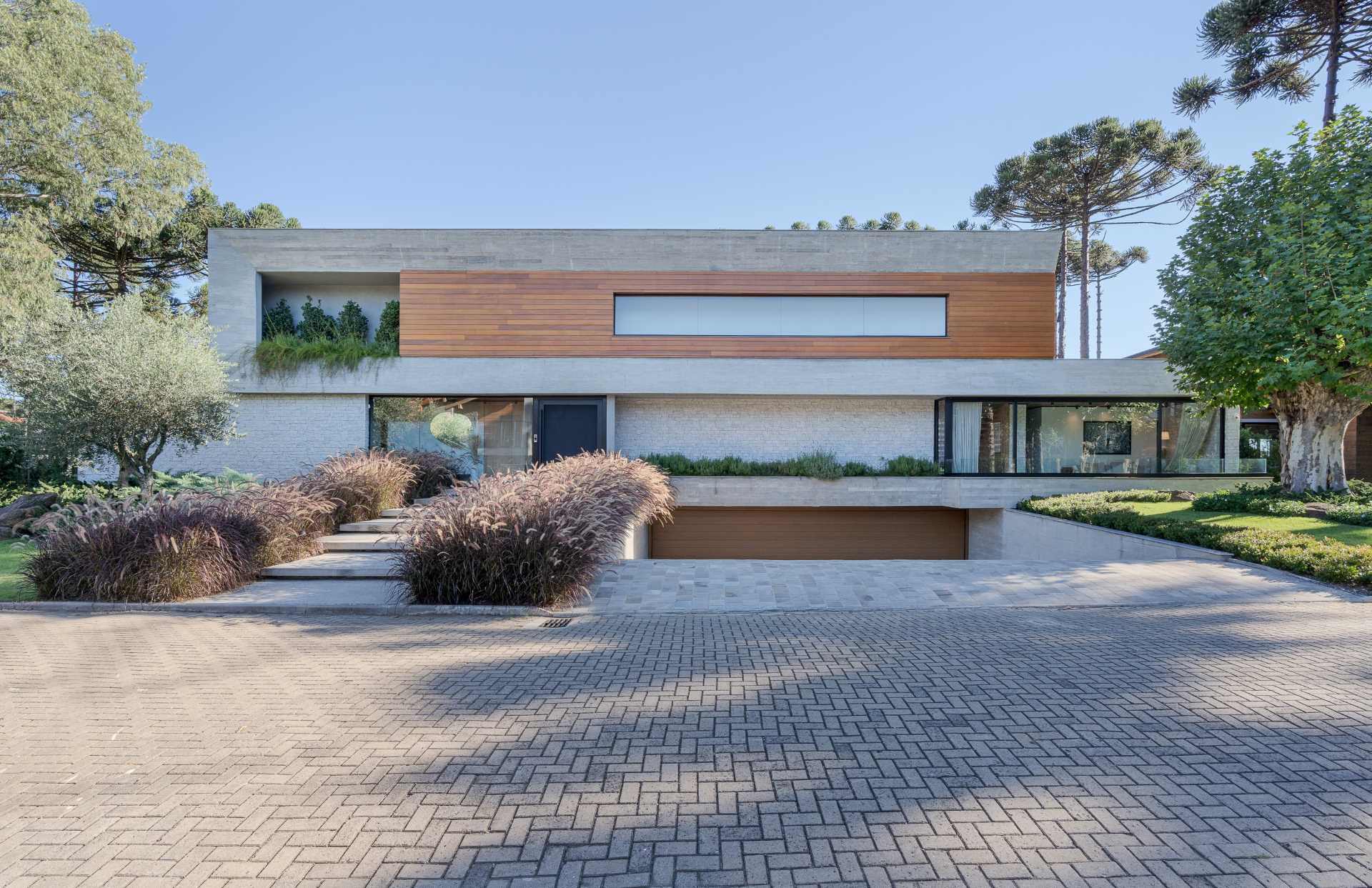The facade of the home showcases concrete, wood, and stone, as well as a sunken garage and a stepped pathway lined with plants.