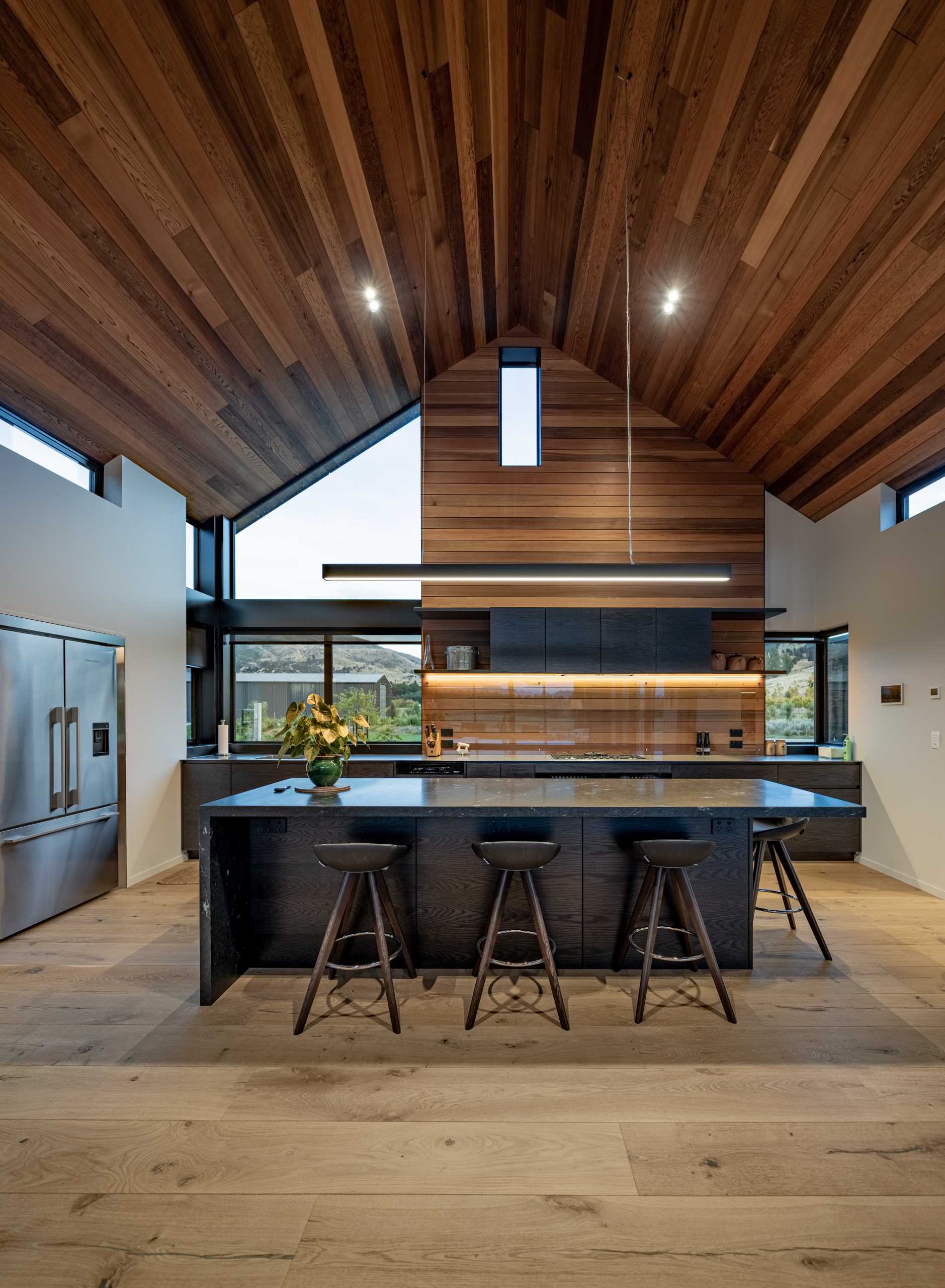 In this modern kitchen, the dark cabinets contrast the wood on the ceiling and walls, while a glass backsplash protects the wood, and hidden lighting highlights it.