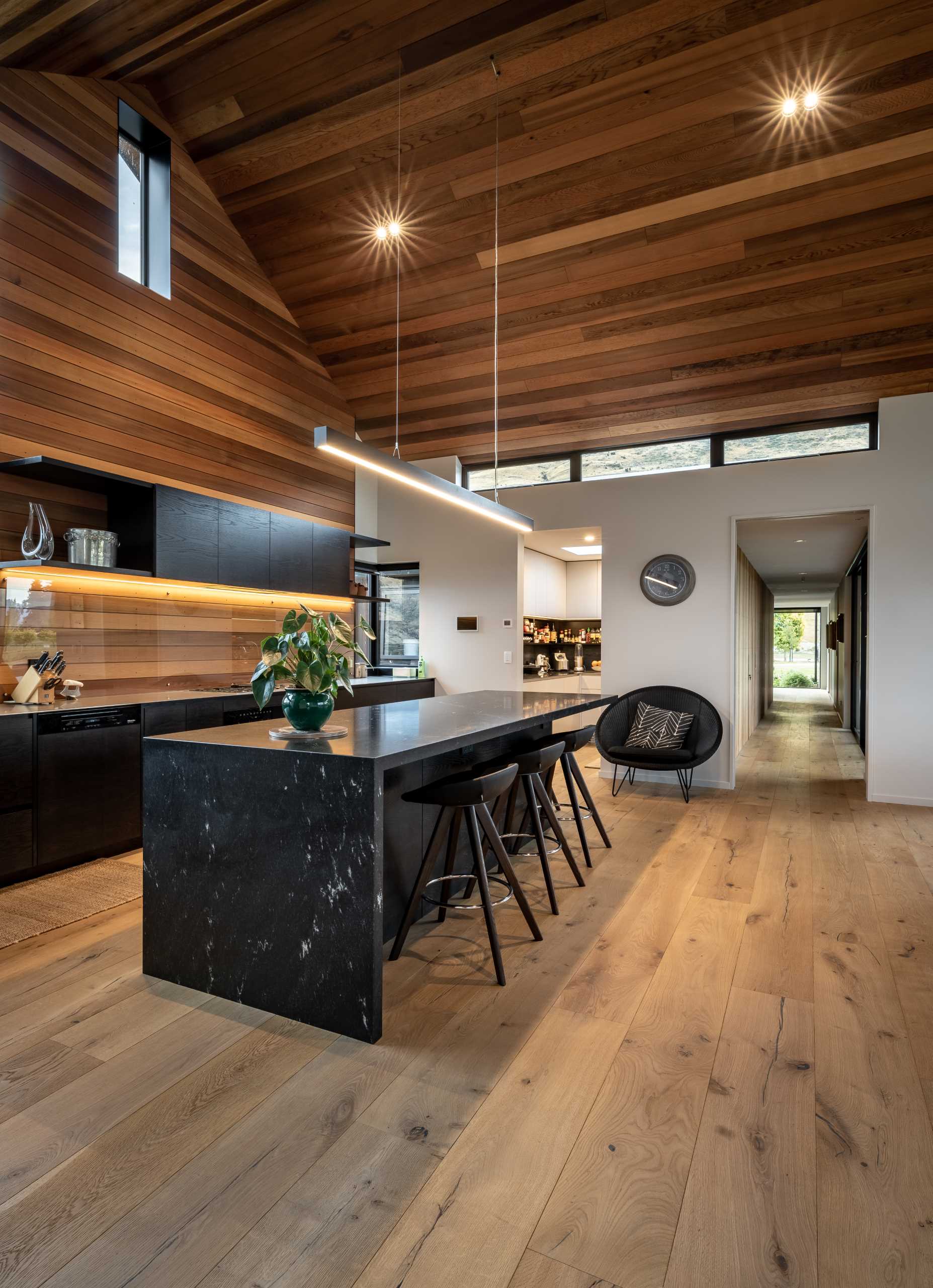 In this modern kitchen, the dark cabinets contrast the wood on the ceiling and walls, while a glass backsplash protects the wood, and hidden lighting highlights it.