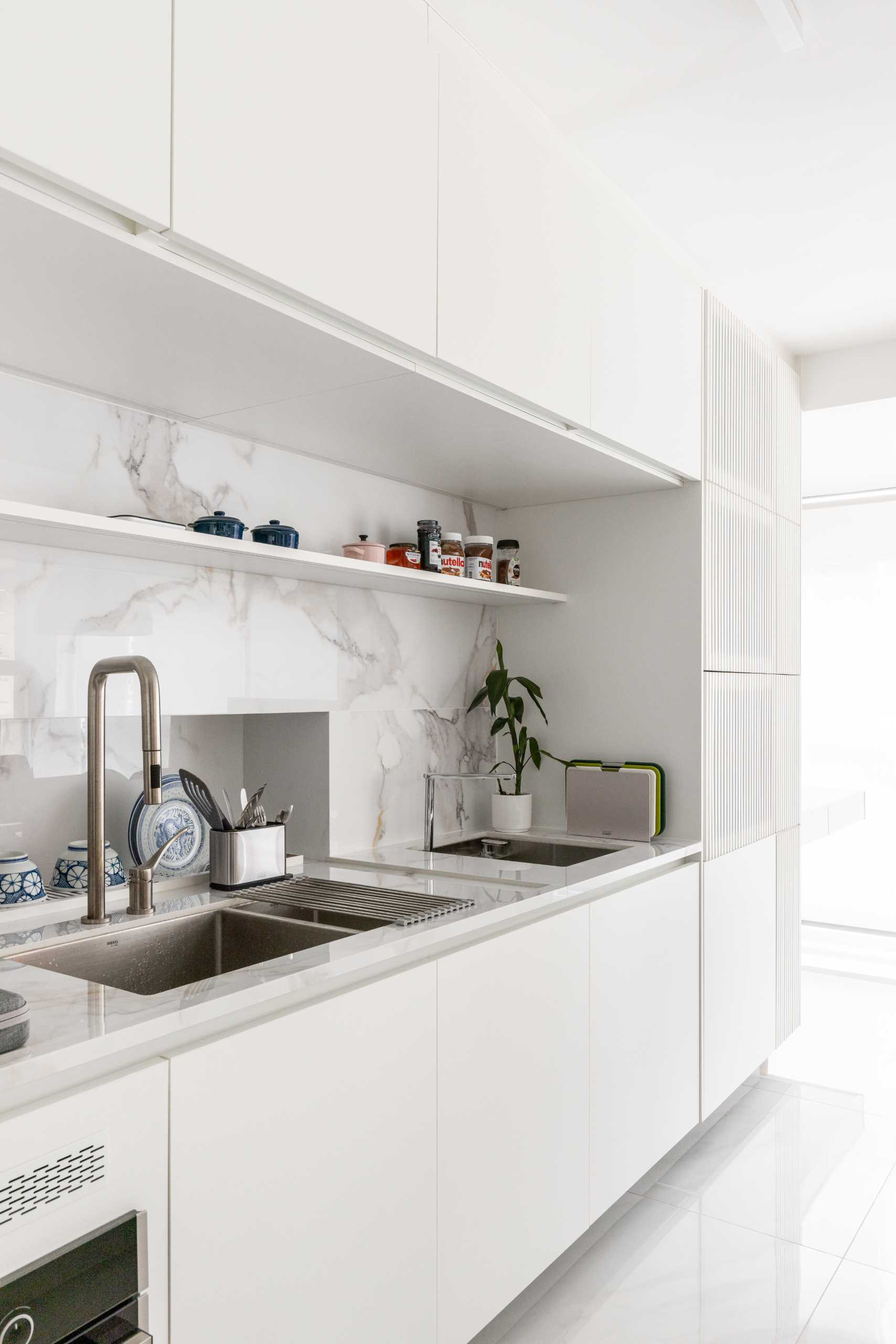 A modern white kitchen with marbled backsplash.