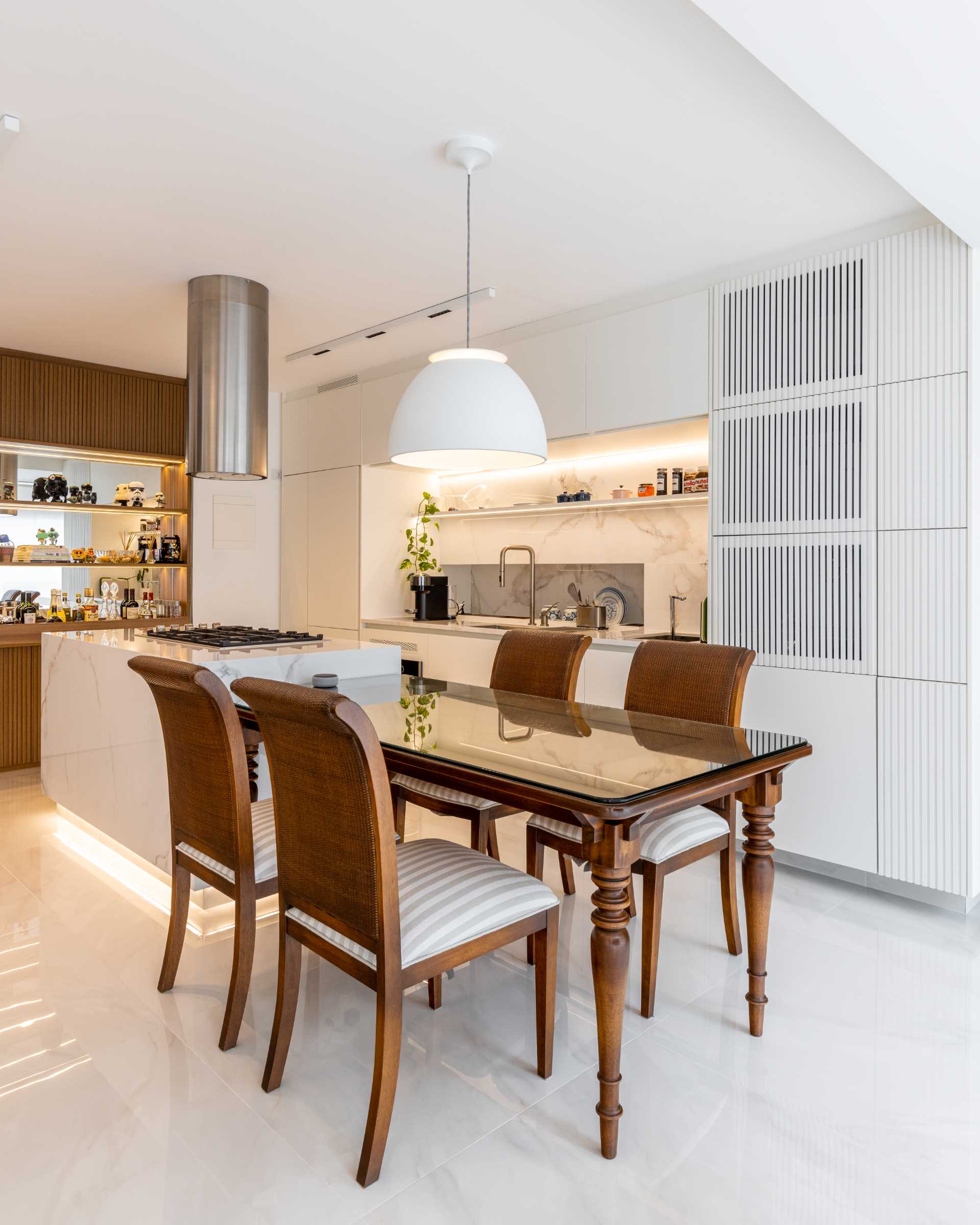A modern kitchen includes wood details, a large island with an adjacent dining table, and hidden lighting.