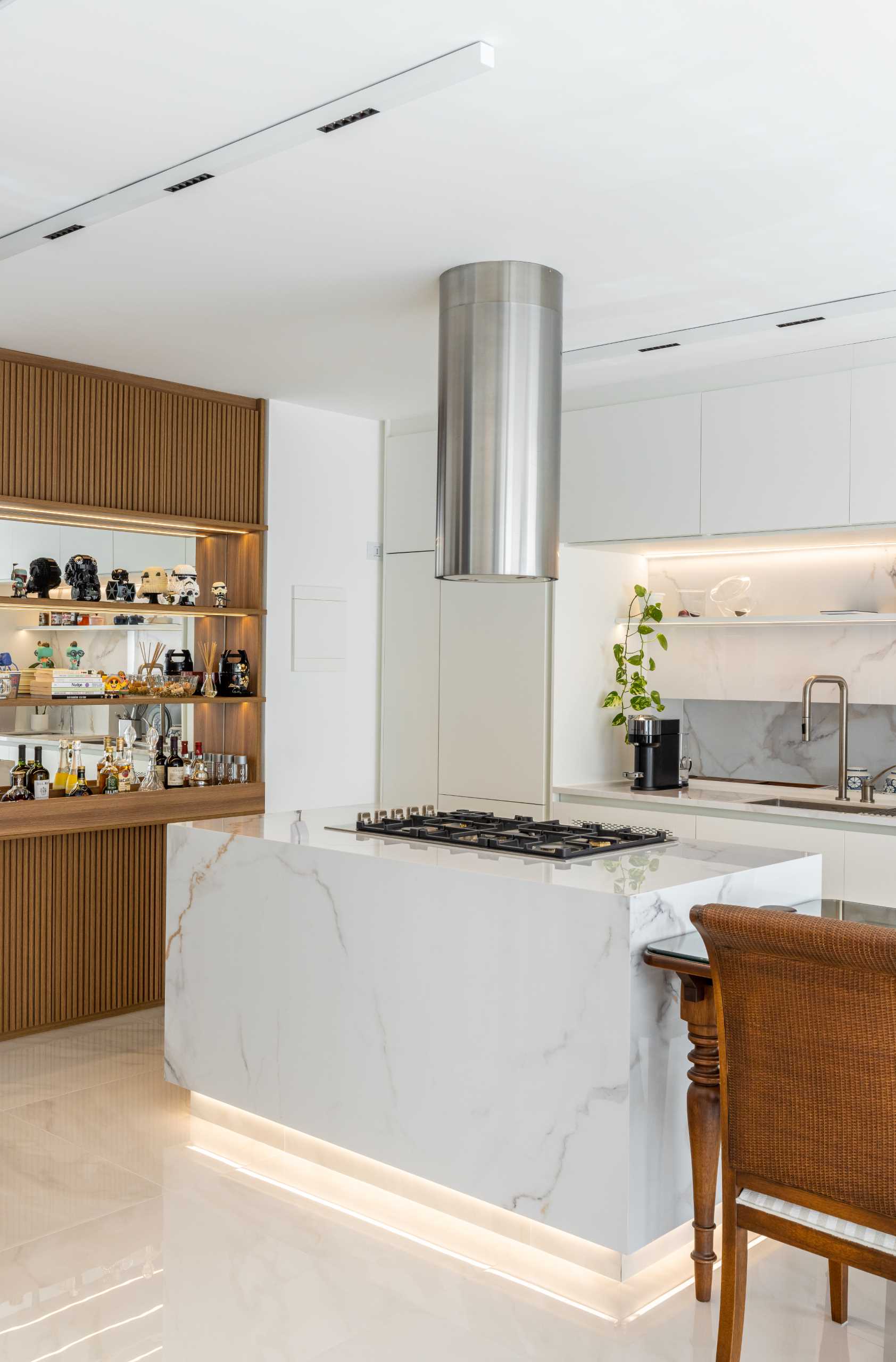 A modern kitchen includes wood details, a large island with an adjacent dining table, and hidden lighting.