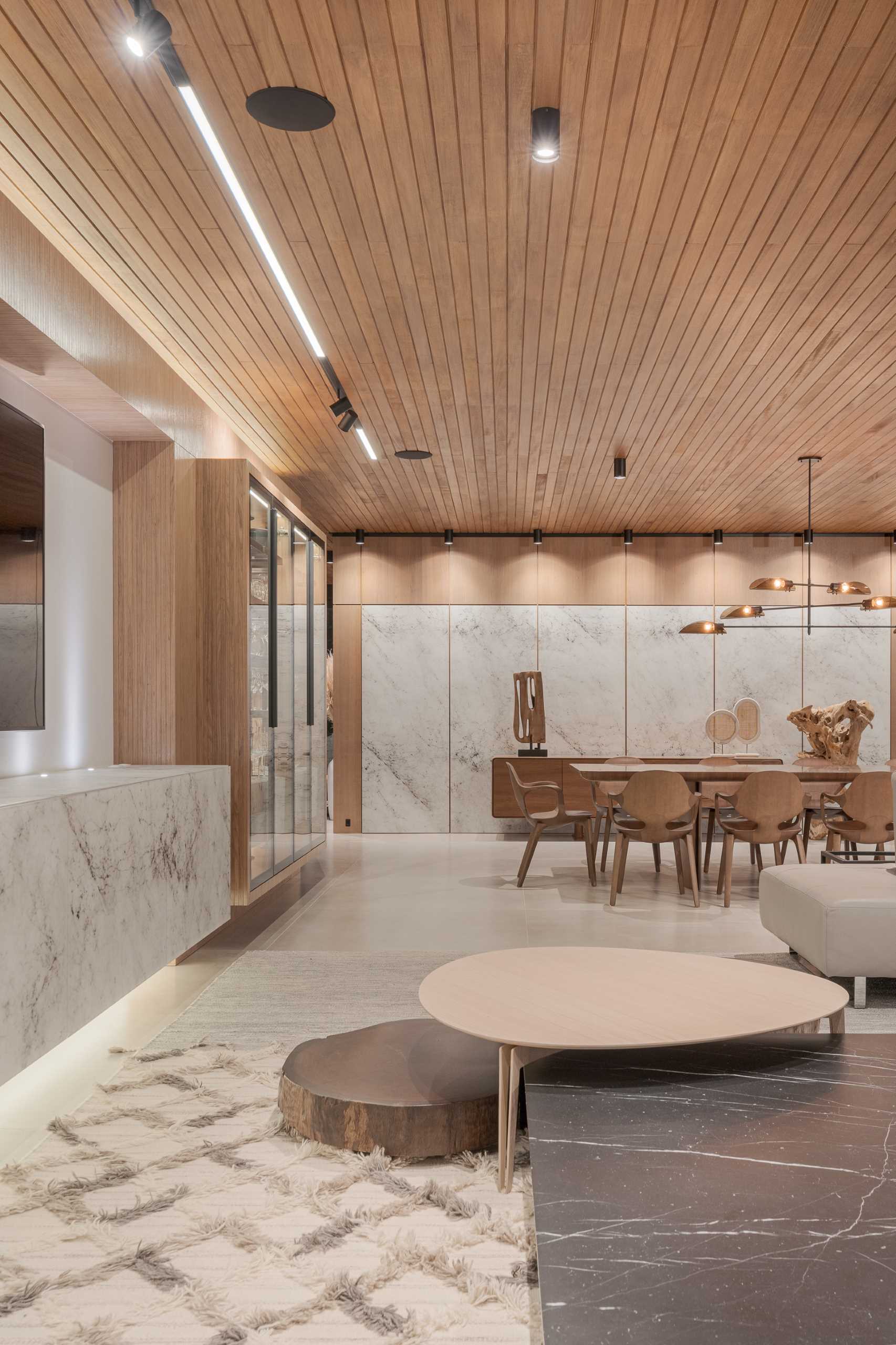 A built-in cabinet with glass doors stores complements this modern dining area, while the wall features stone panels and a wood sideboard.