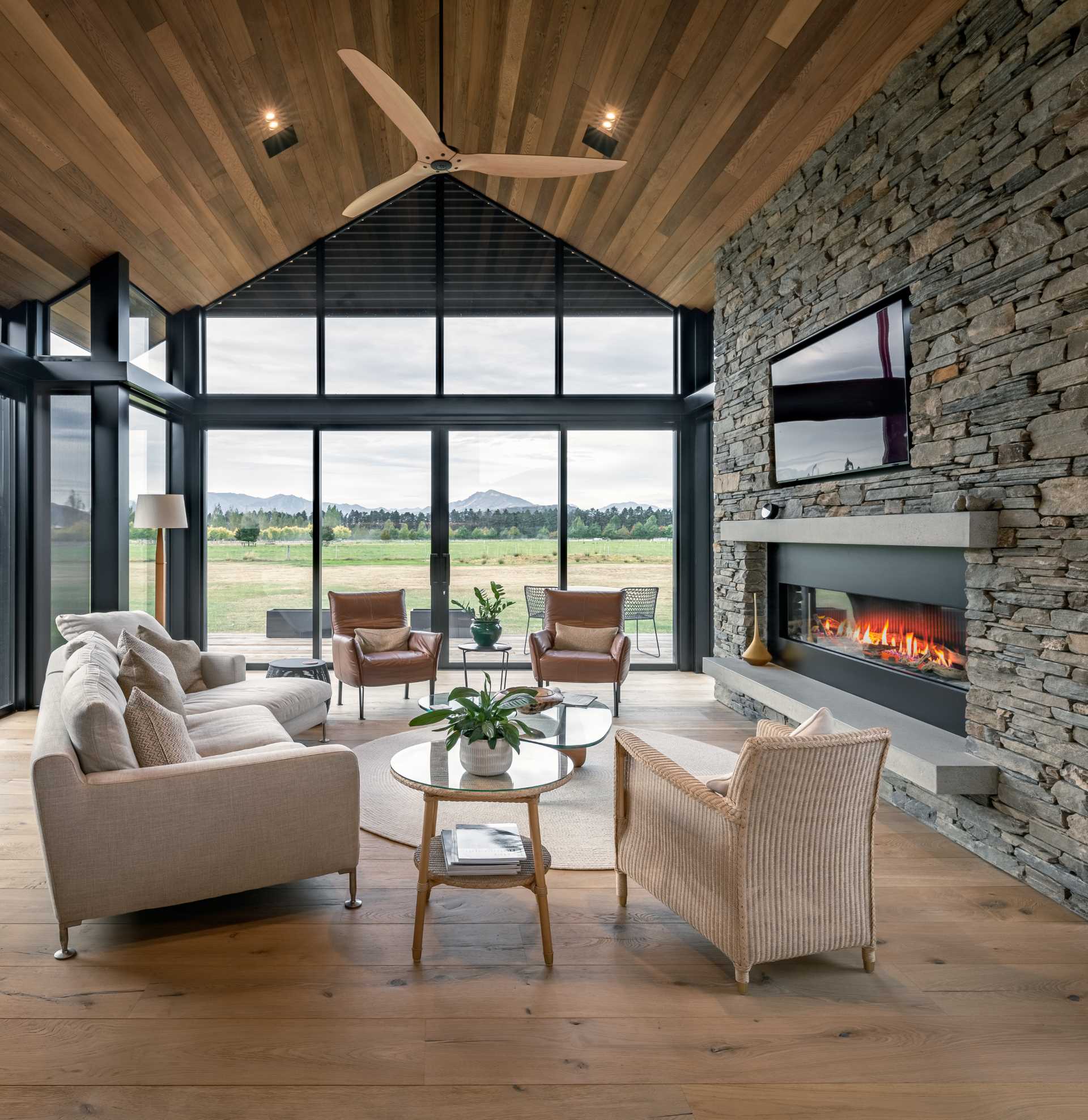 This modern living room has timber-lined walls and ceilings, hardwood floors, and a chunky schist fireplace.