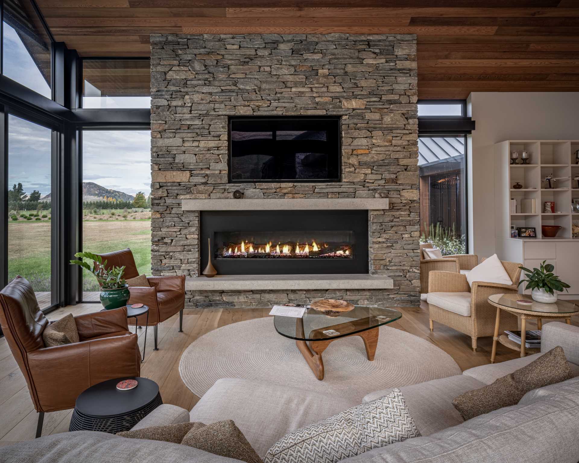 This modern living room has timber-lined walls and ceilings, hardwood floors, and a chunky schist fireplace.