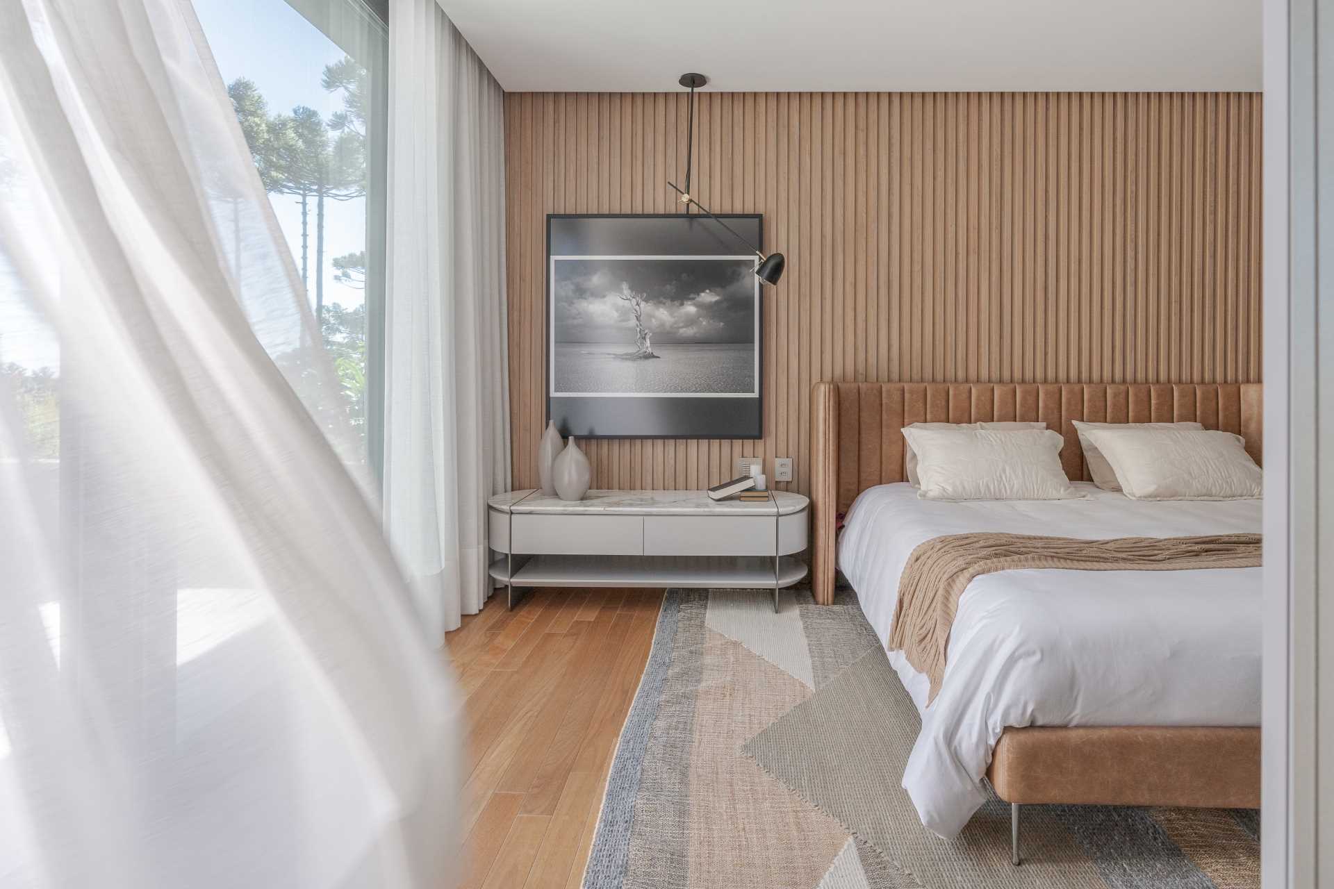 In this modern primary bedroom, vertical wood strips line the wall, while the bed has a curved padded headboard.