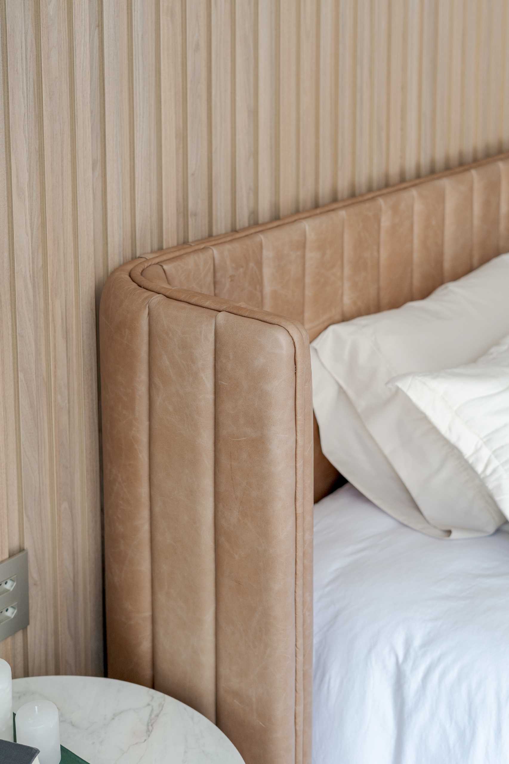 In this modern primary bedroom, vertical wood strips line the wall, while the bed has a curved padded headboard.