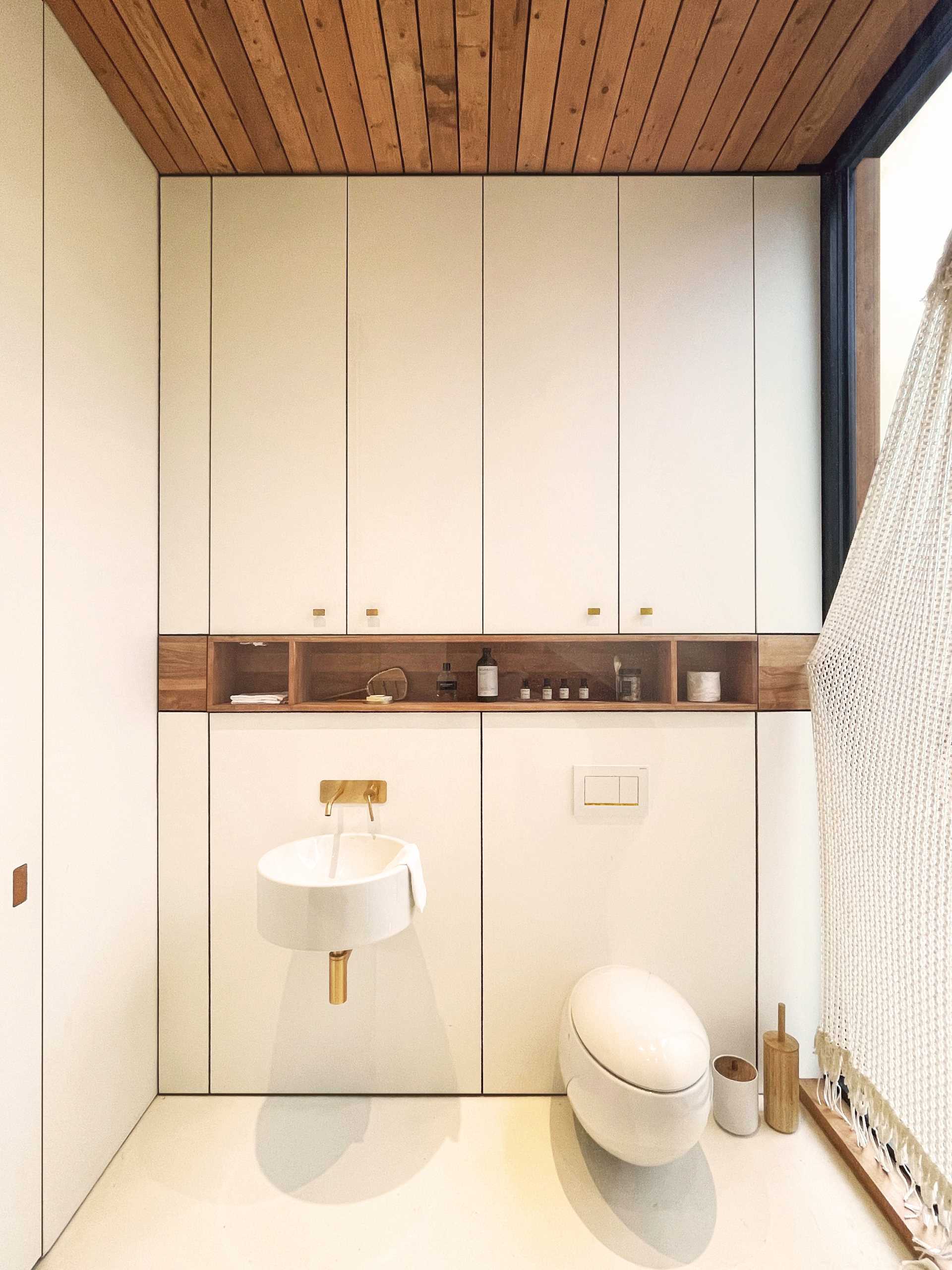 A modern bathroom with minimalist cabinets, a wood shelving niche, and bronze hardware.