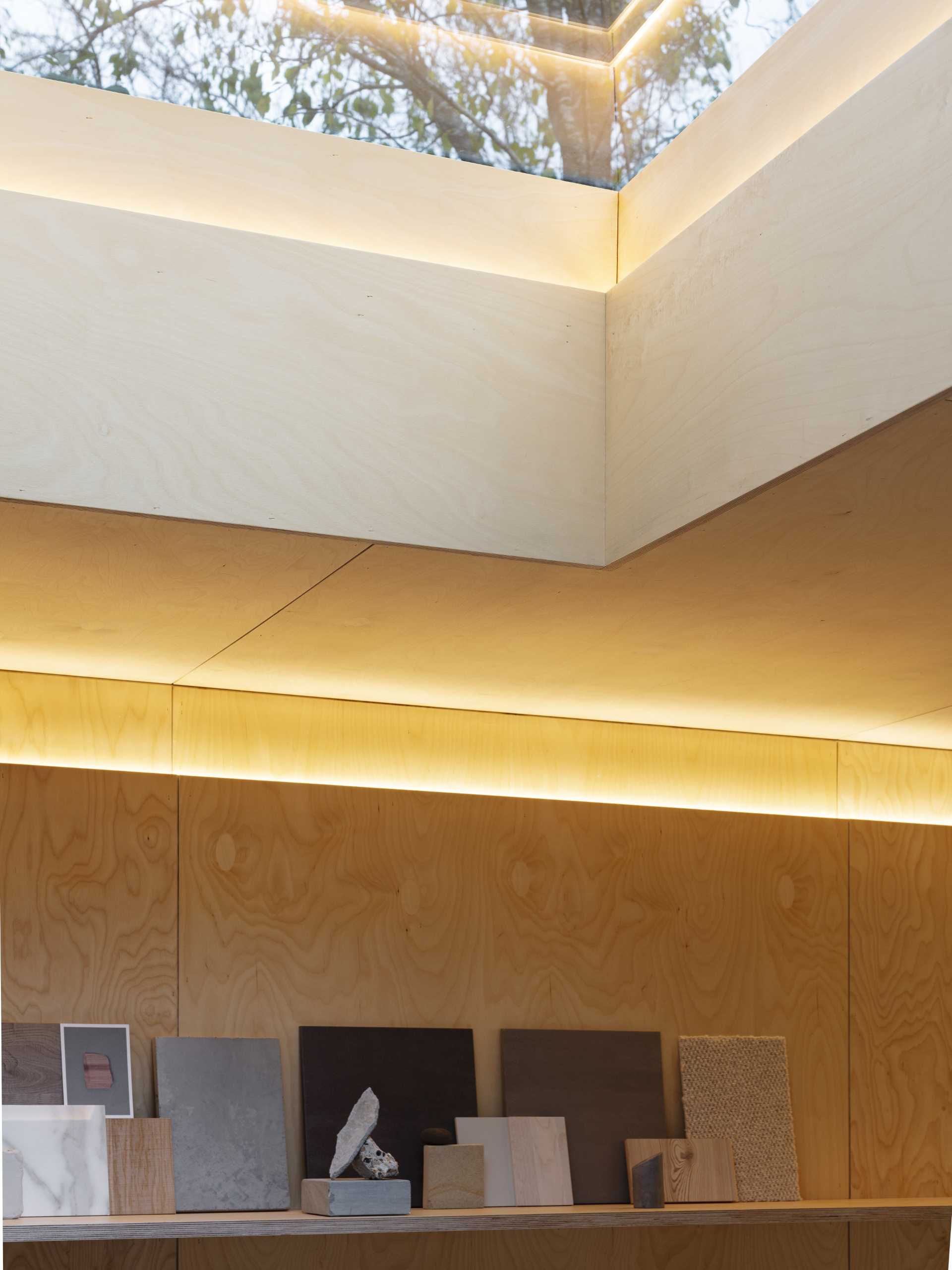 A skylight adds natural light to this backyard studio, while a shelf wrap around the wall from the kitchen to the bookshelf.