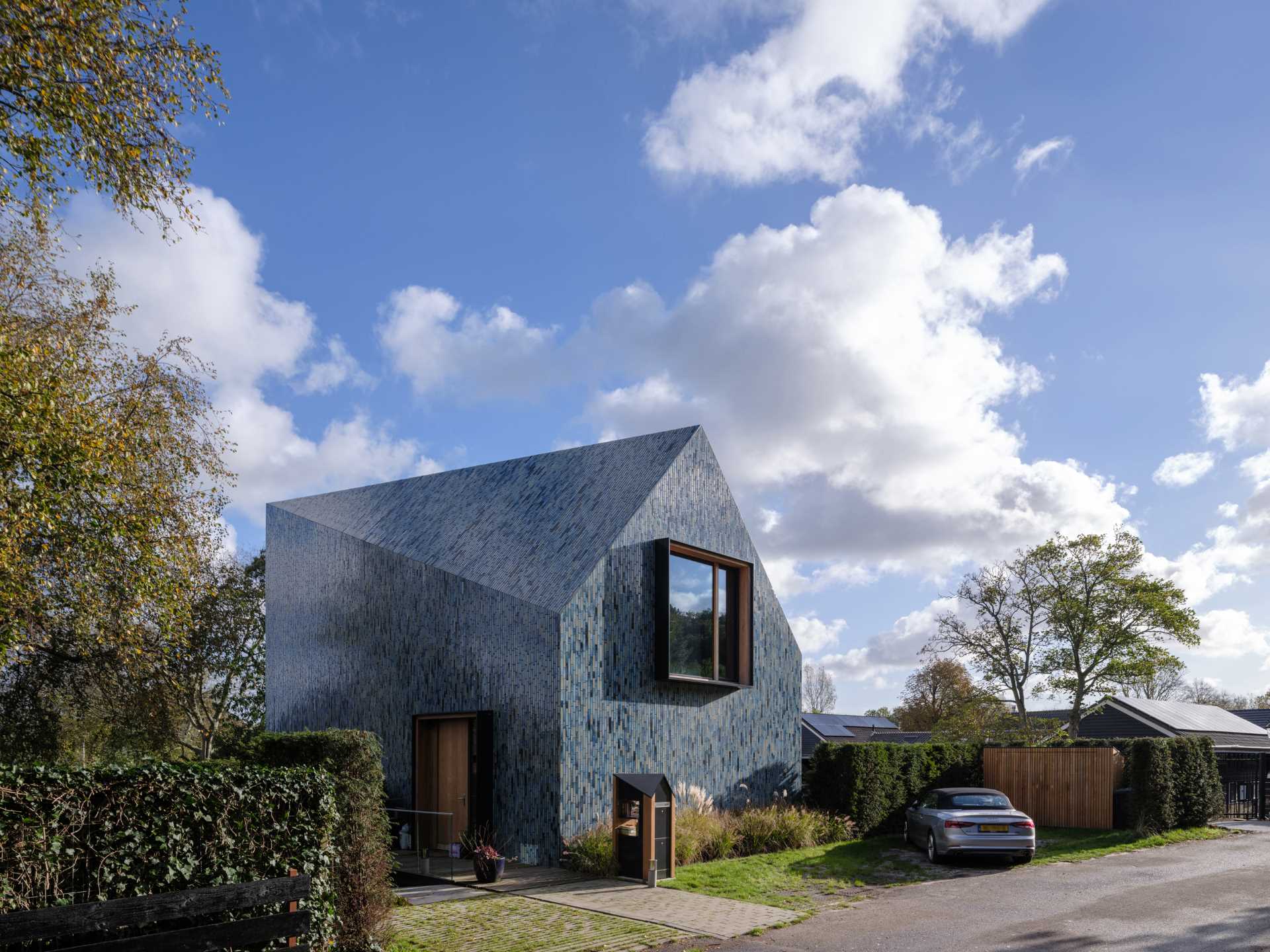 A modern house covered in blue tiles, that also has a twisted roof.