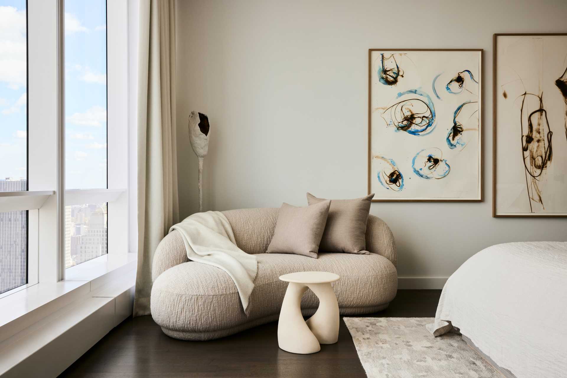 A modern bedroom with a neutral color palette and small sitting area.