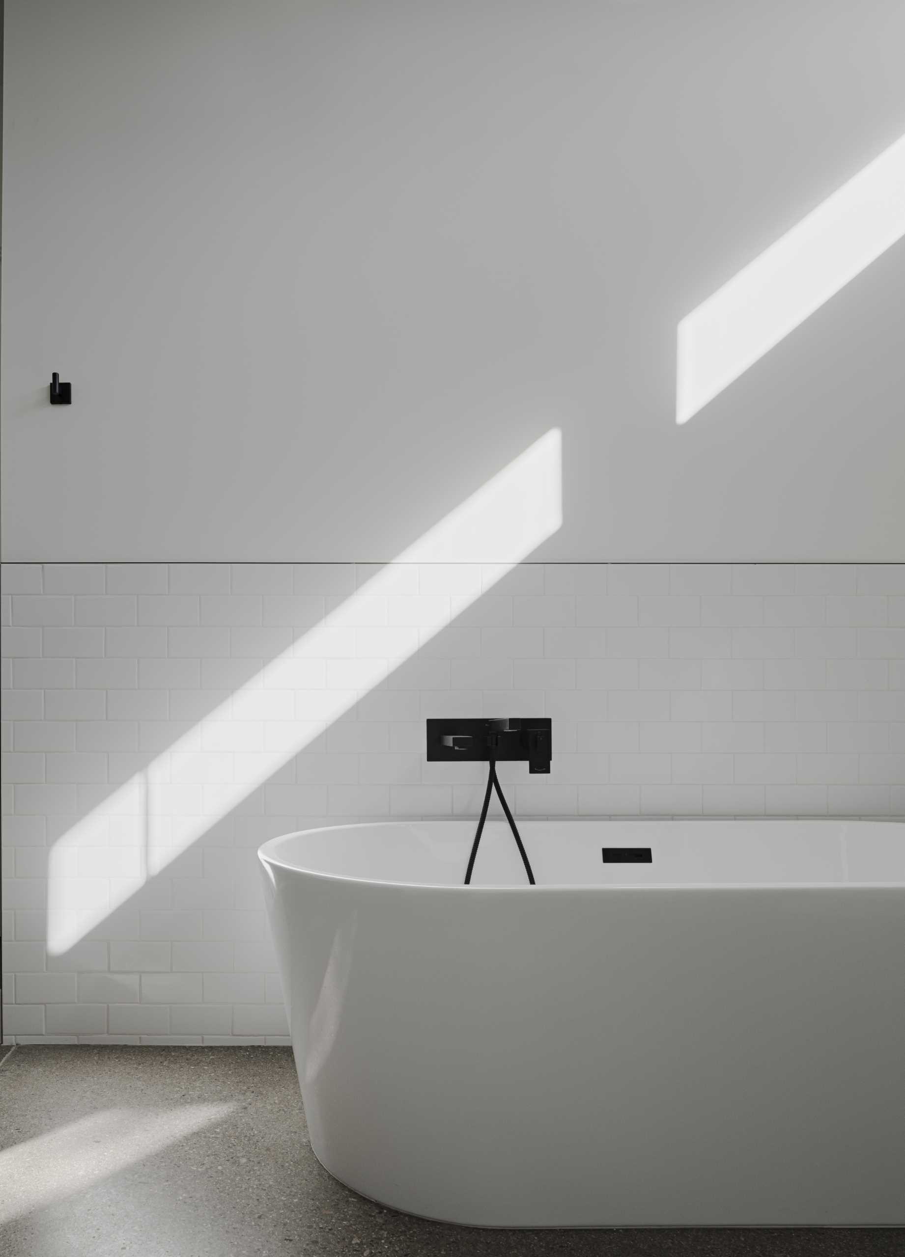 A white bathroom with freestanding bathtub includes black accents.