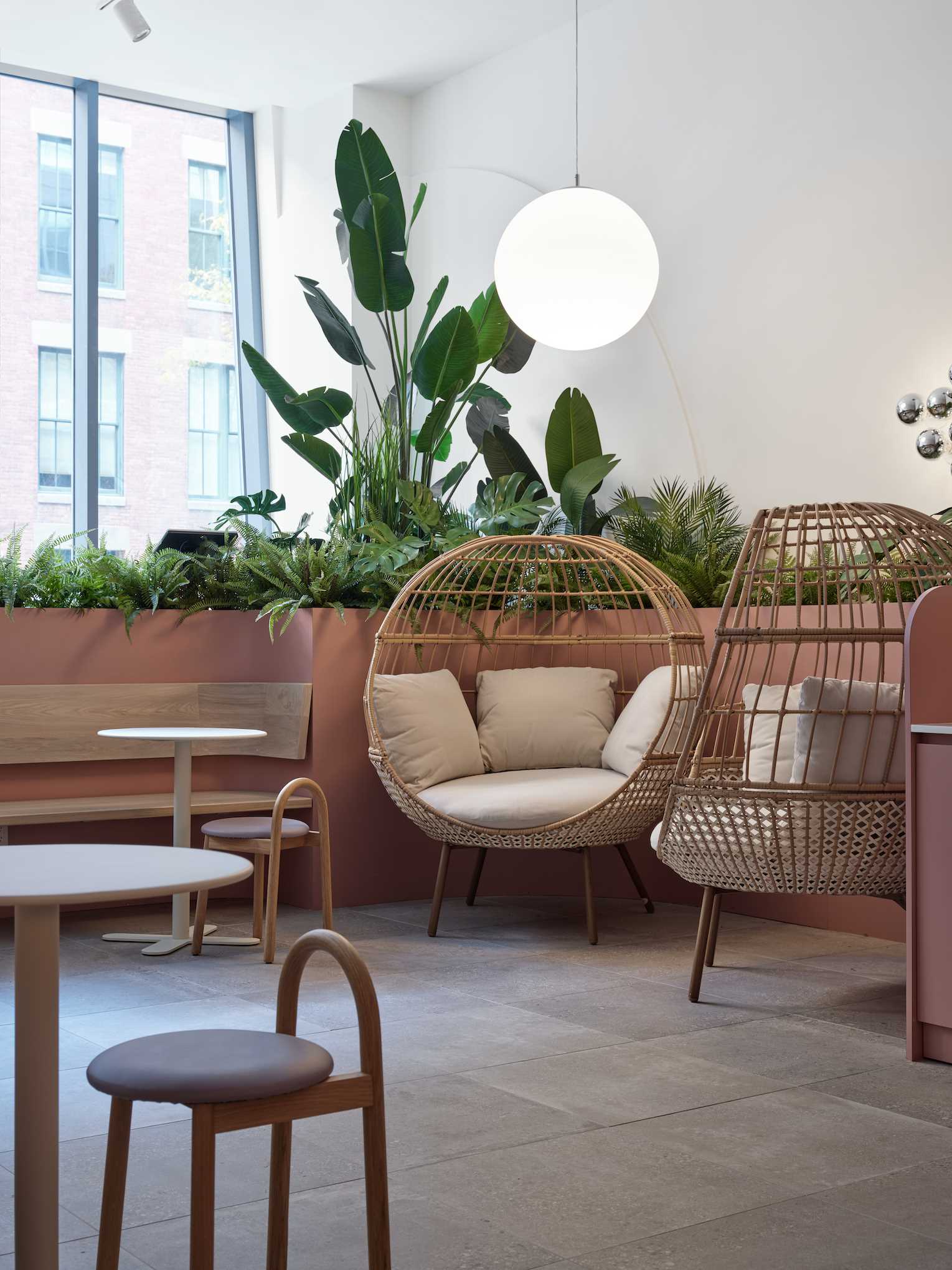 A modern cafe with plants, cozy seating, and soft colors.