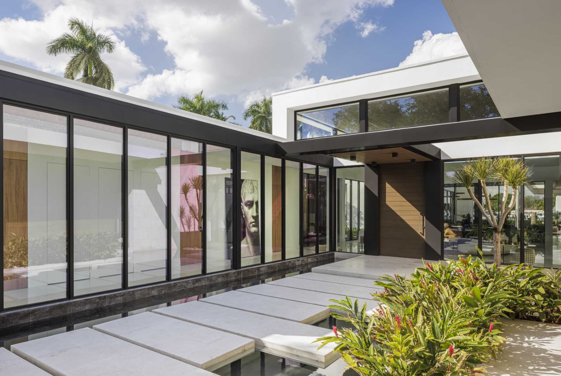 A series of floating concrete steps lead across a pond and guide visitors to the front door. Floor-to-ceiling windows provide a glimpse of the interior.