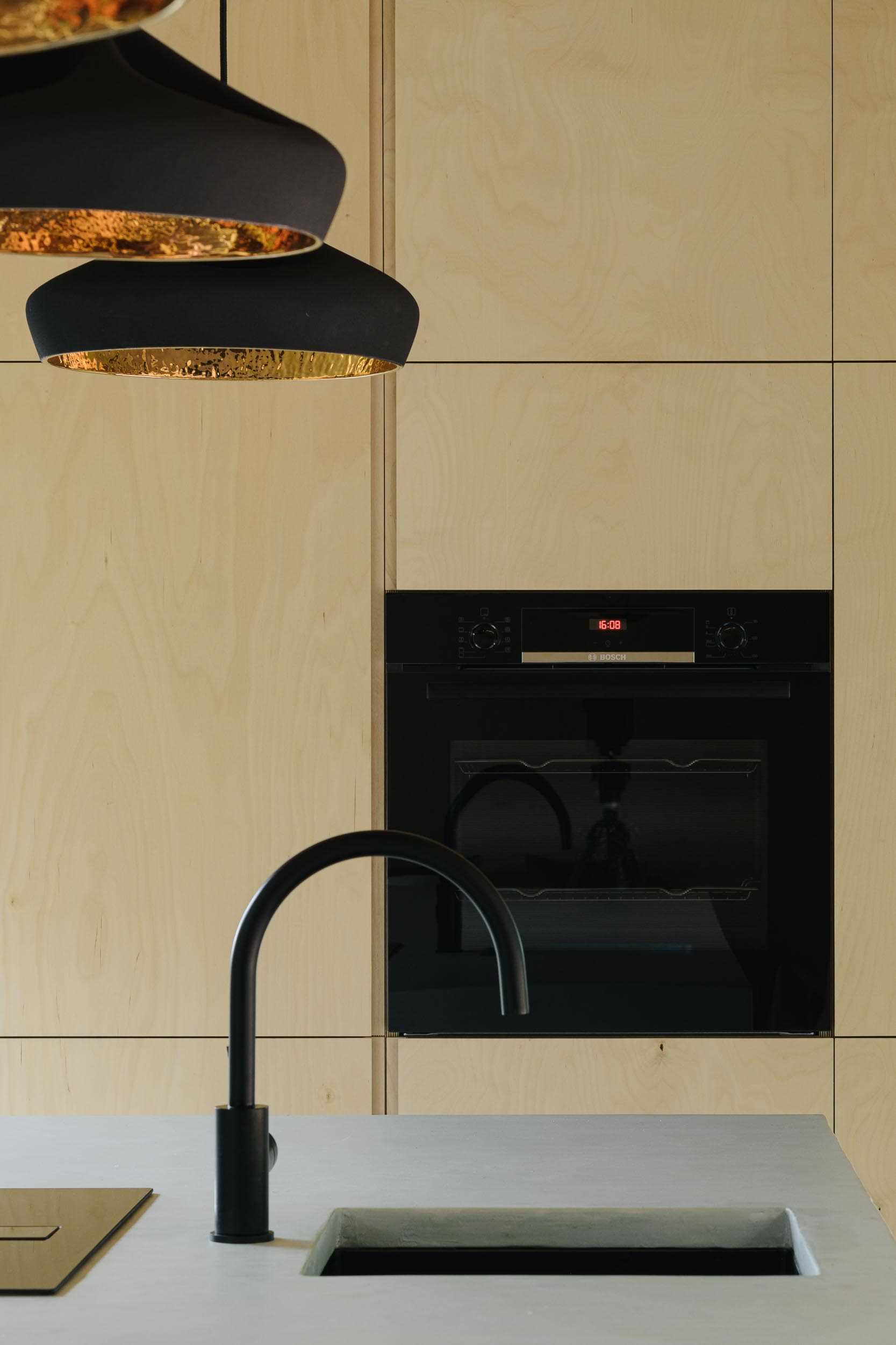 A modern kitchen includes birch plywood cabinets and black pendant lighting.