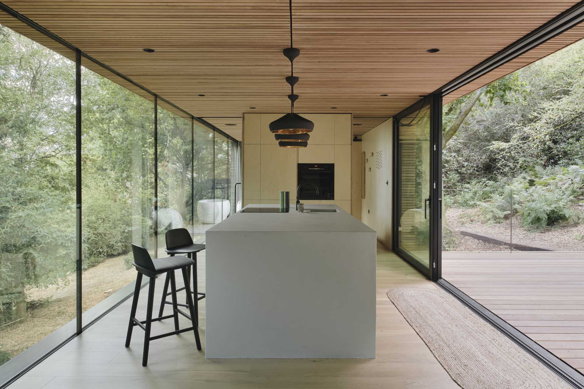 یک آشپزخانه مدرن شامل کابینت های تخته سه لا توس و نور آویز مشکی است.