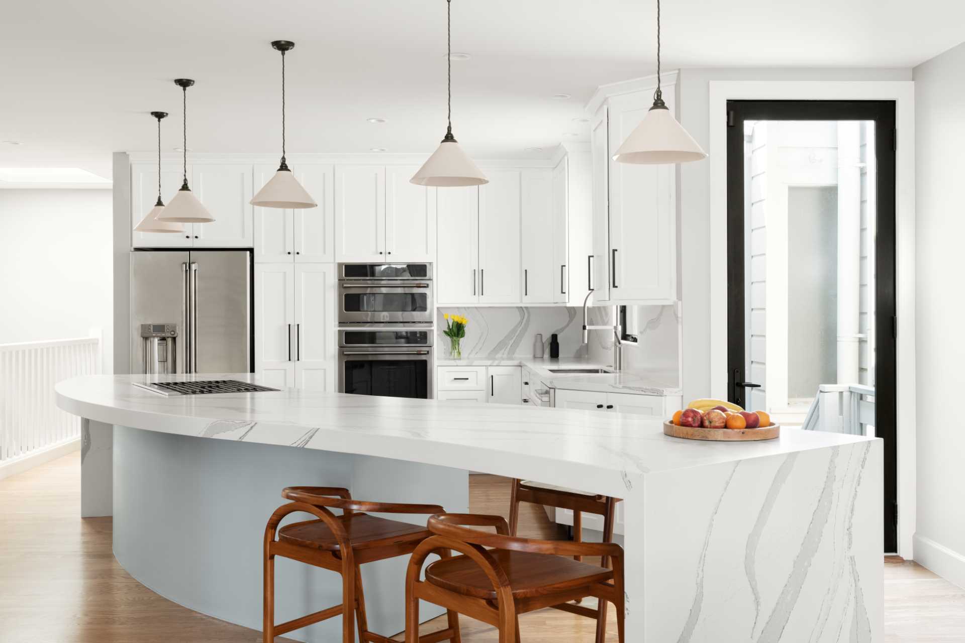 A hint of color has been added in this kitchen with lower cabinets in the island, while a down draft, telescoping hood allows the range to be placed in the serpentine island. The shape of the kitchen island also allows for a section of it to be dedicated to seating.