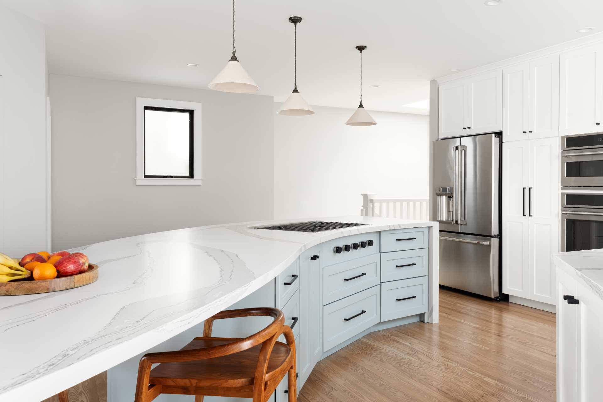 A hint of color has been added in this kitchen with lower cabinets in the island, while a down draft, telescoping hood allows the range to be placed in the serpentine island. The shape of the kitchen island also allows for a section of it to be dedicated to seating.
