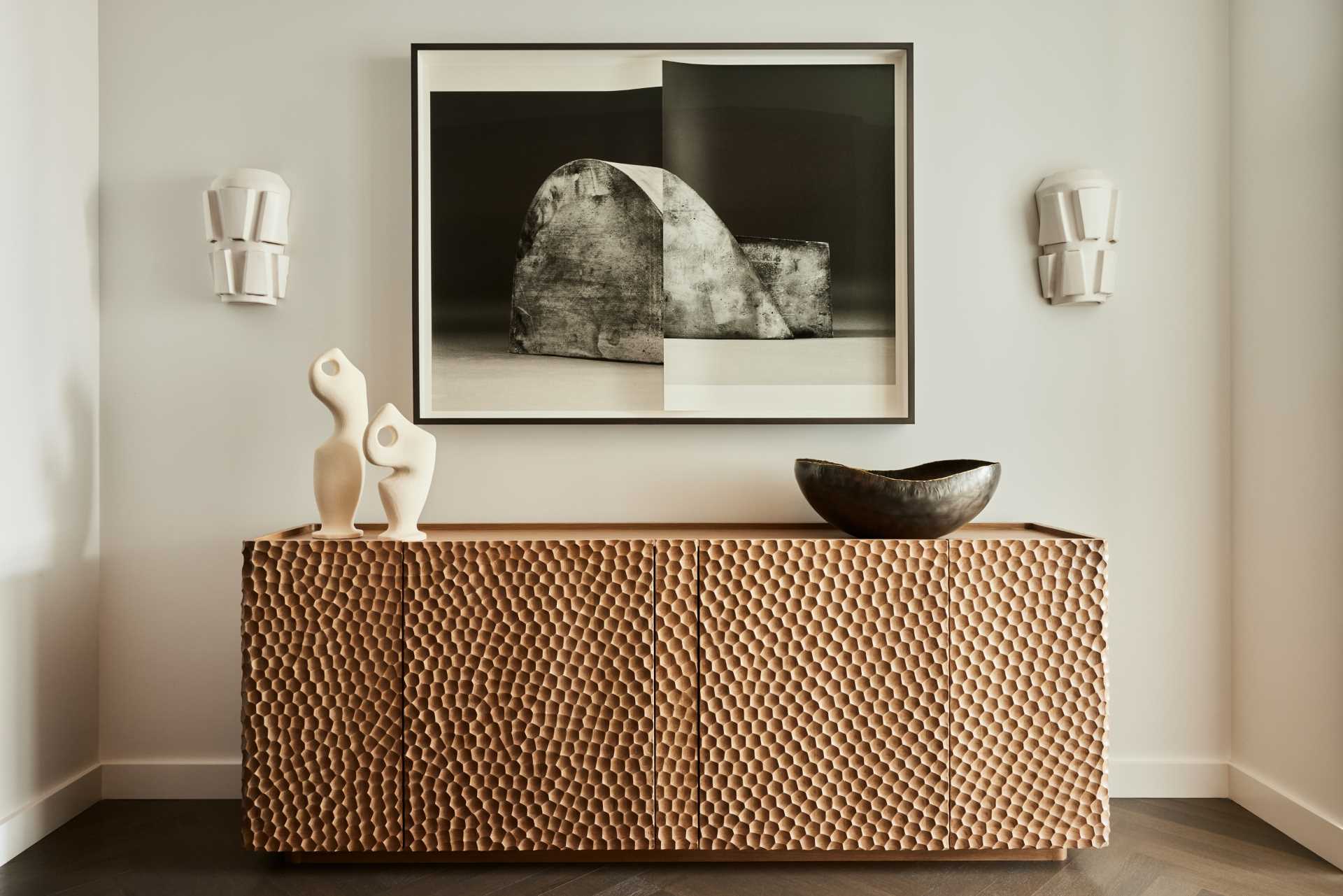 A gouged wood credenza has Erin Schirreff art hanging above and ceramic sconces from The Invisible Collection.