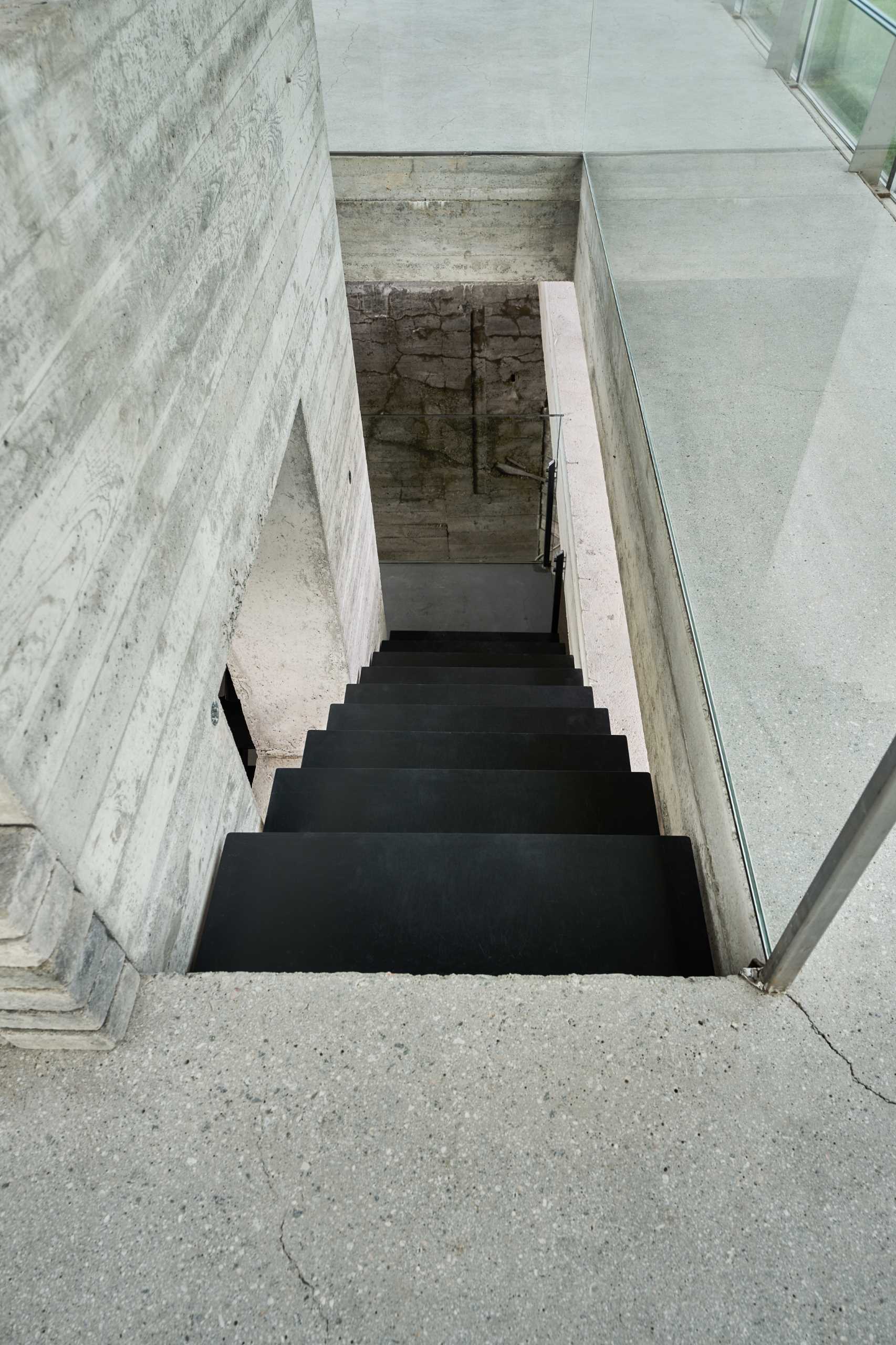 Black metal stairs contrast the concrete walls and glass railings.