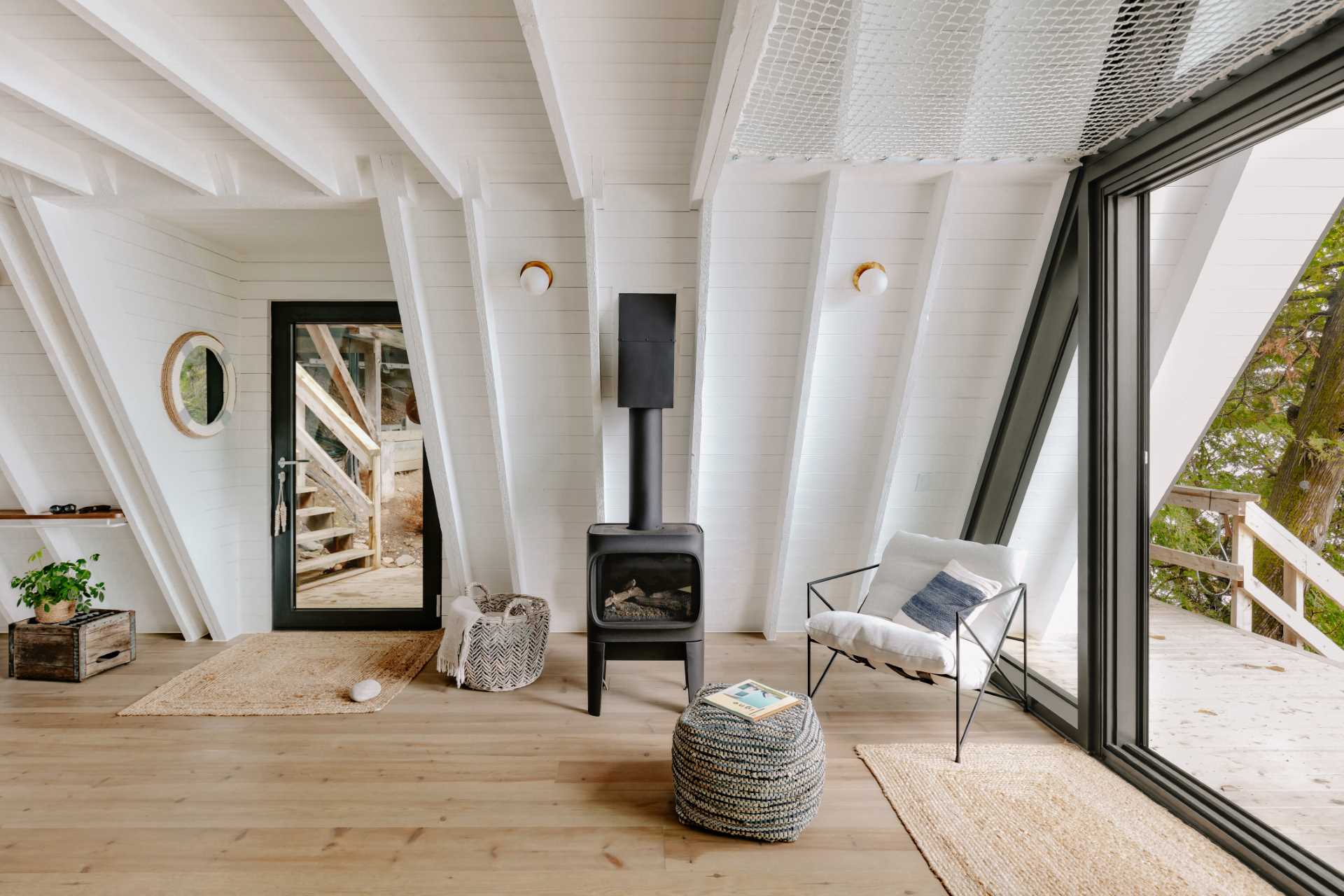 A updated A-Frame cabin with a white interior, wood floors, and a living room that includes a fireplace and opens to a deck.