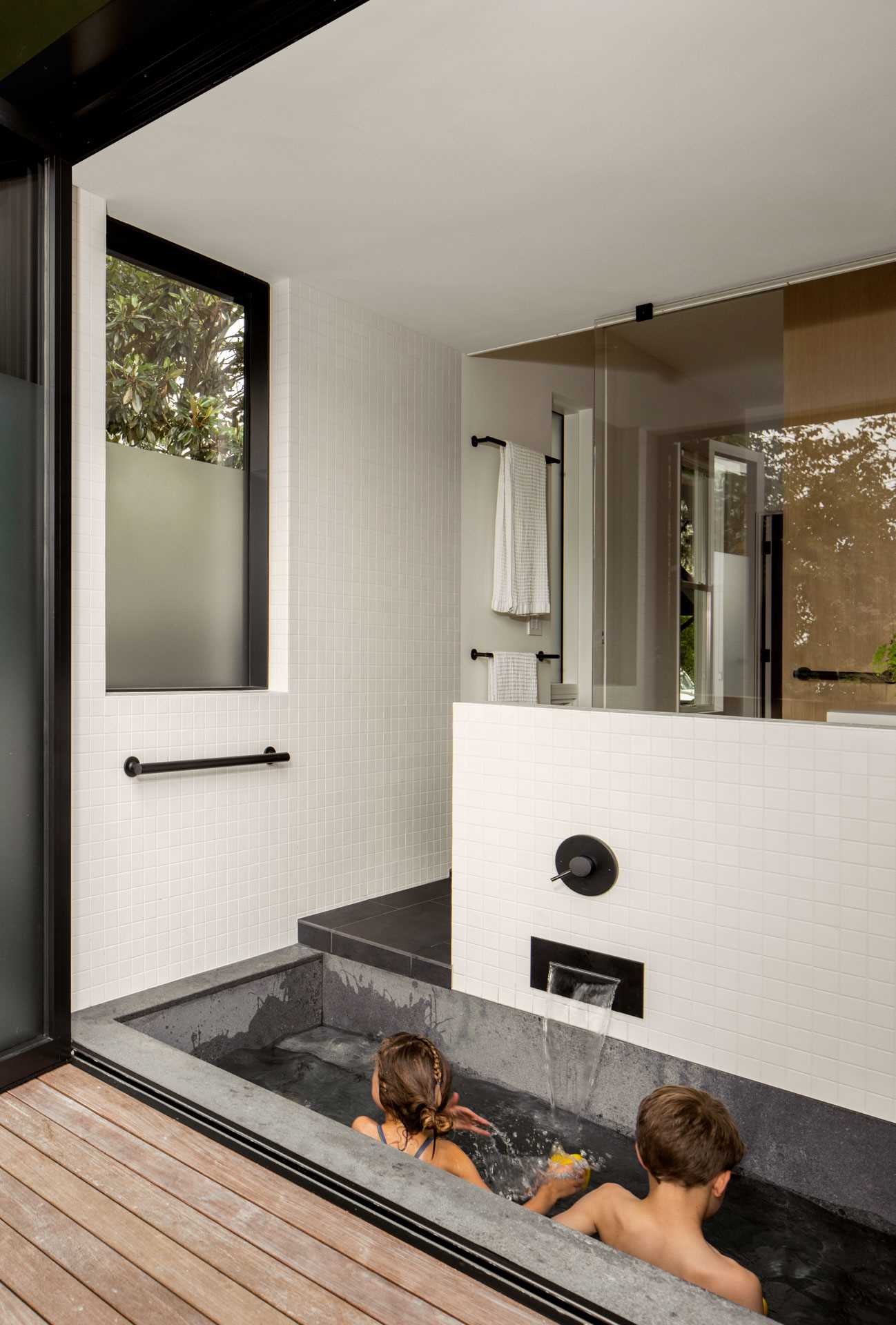 A modern family bathroom includes a traditional Japanese soaking tub (Ofuro), directly connecting to the outdoors via a folding glass door. A separate toilet room increases comfort and usability for the young family.