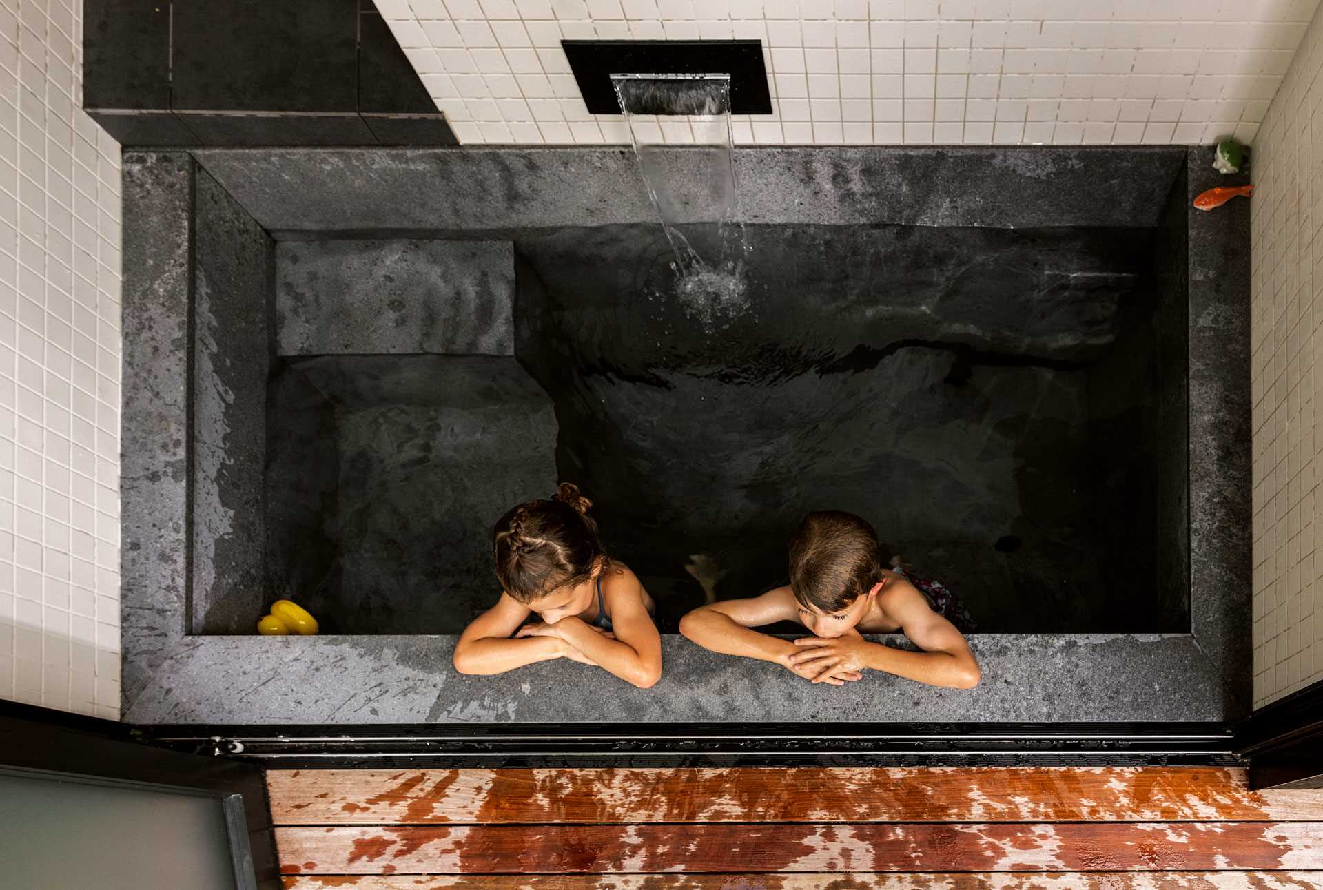 A modern family bathroom includes a traditional Japanese soaking tub (Ofuro), directly connecting to the outdoors via a folding glass door. A separate toilet room increases comfort and usability for the young family.