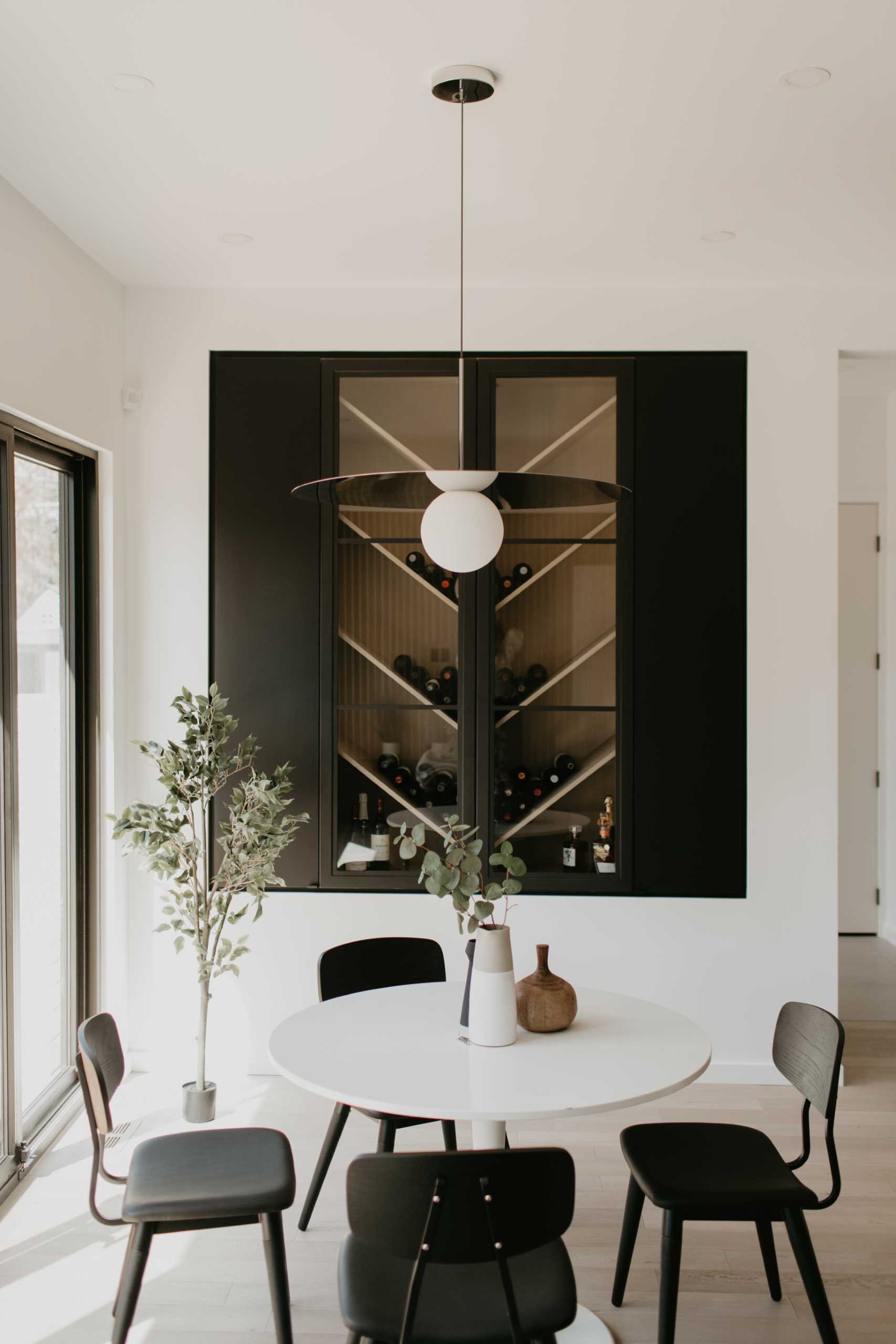 A wine rack with shelves angled in a chevron pattern creates an interesting focal point to this dining area, while a round table is positioned below the minimalist pendant light.