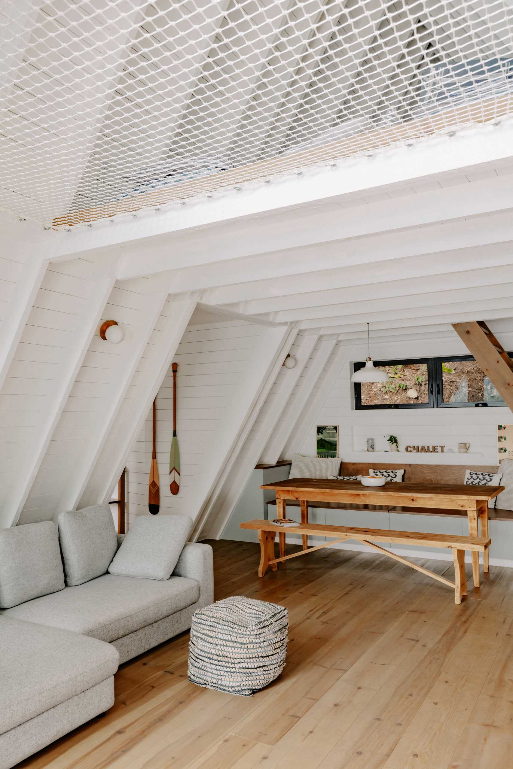 A updated A-Frame cabin with a white interior, wood floors, and banquette seating in the dining area.