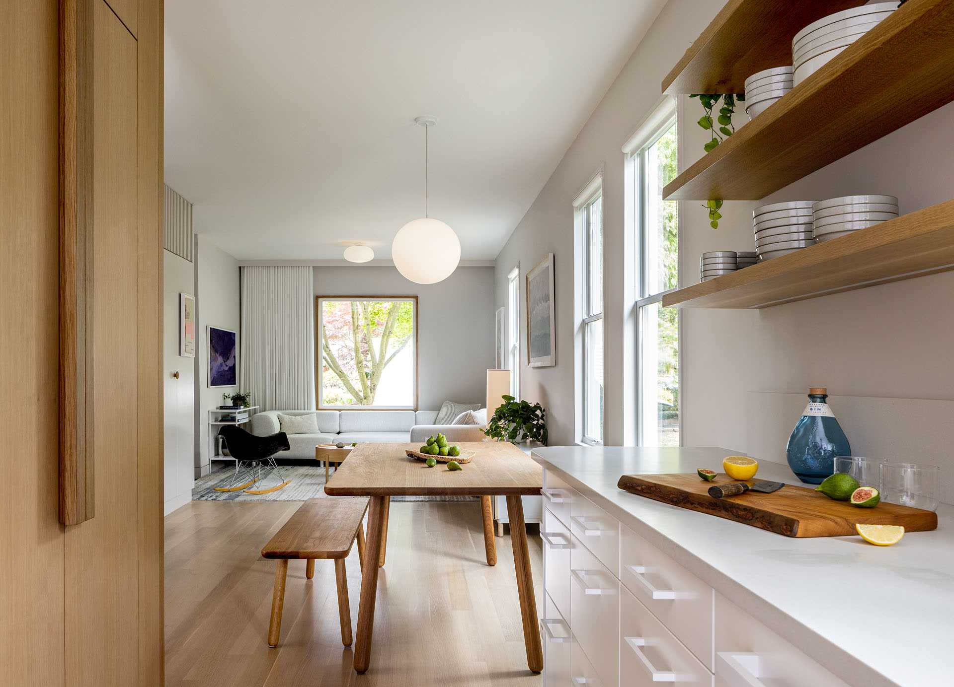 This remodeled living room flows through to the dining room with a wood table and bench seating. A work area with a desk and shelving is located on the opposite wall.