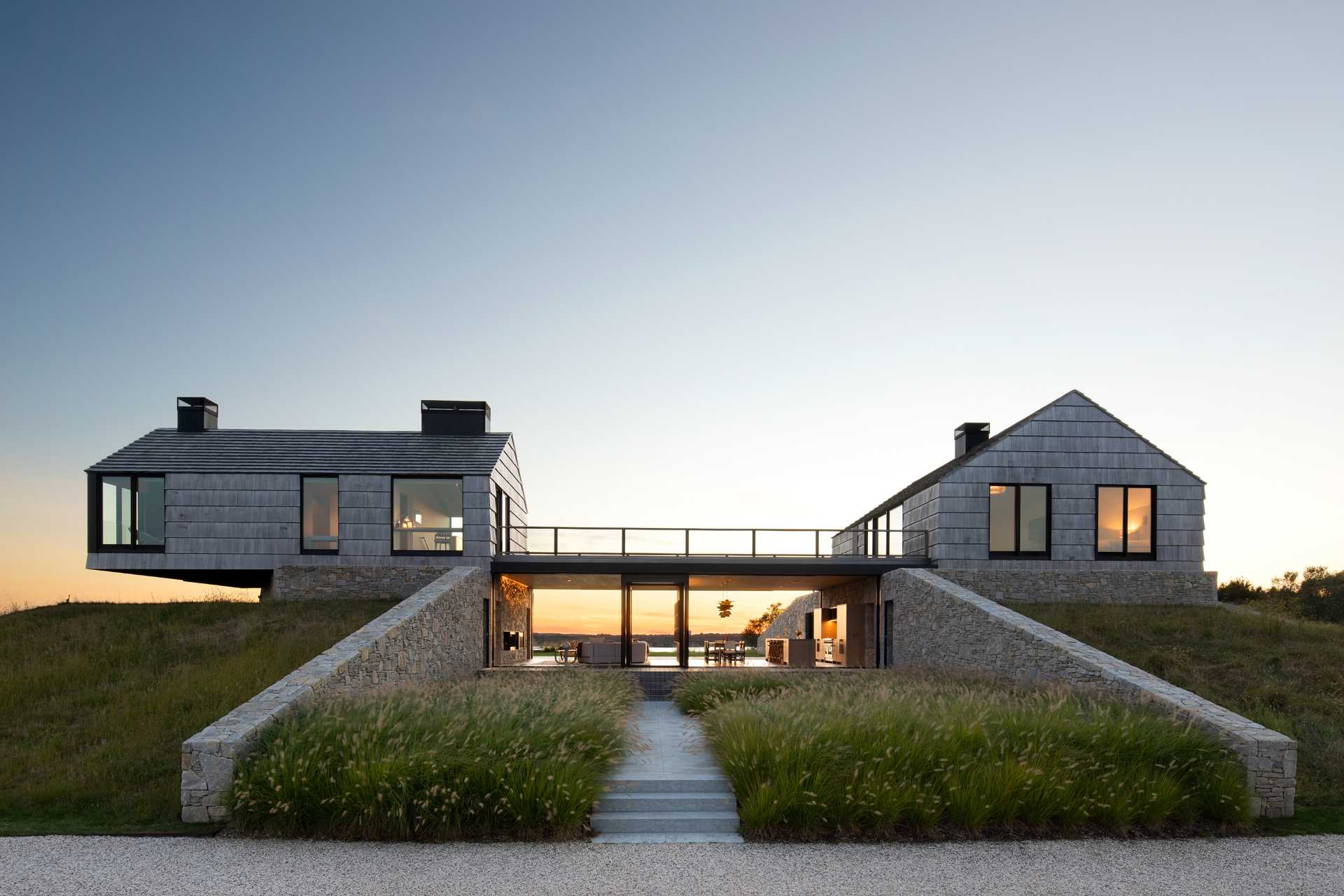 A modern home with two stone and shingle "cottages" connected by an open living room, dining area, and kitchen.