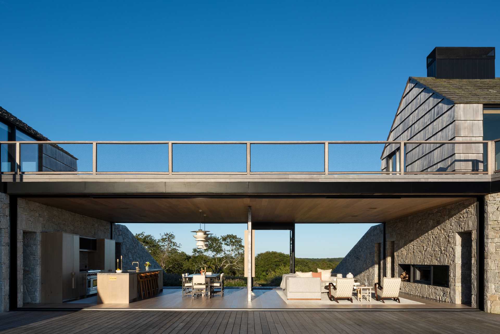 Perched atop the stone walls sit two simple shingled “cottages” reminiscent of the property’s original structures, while between them, is an open plan living room, dining area, and kitchen.