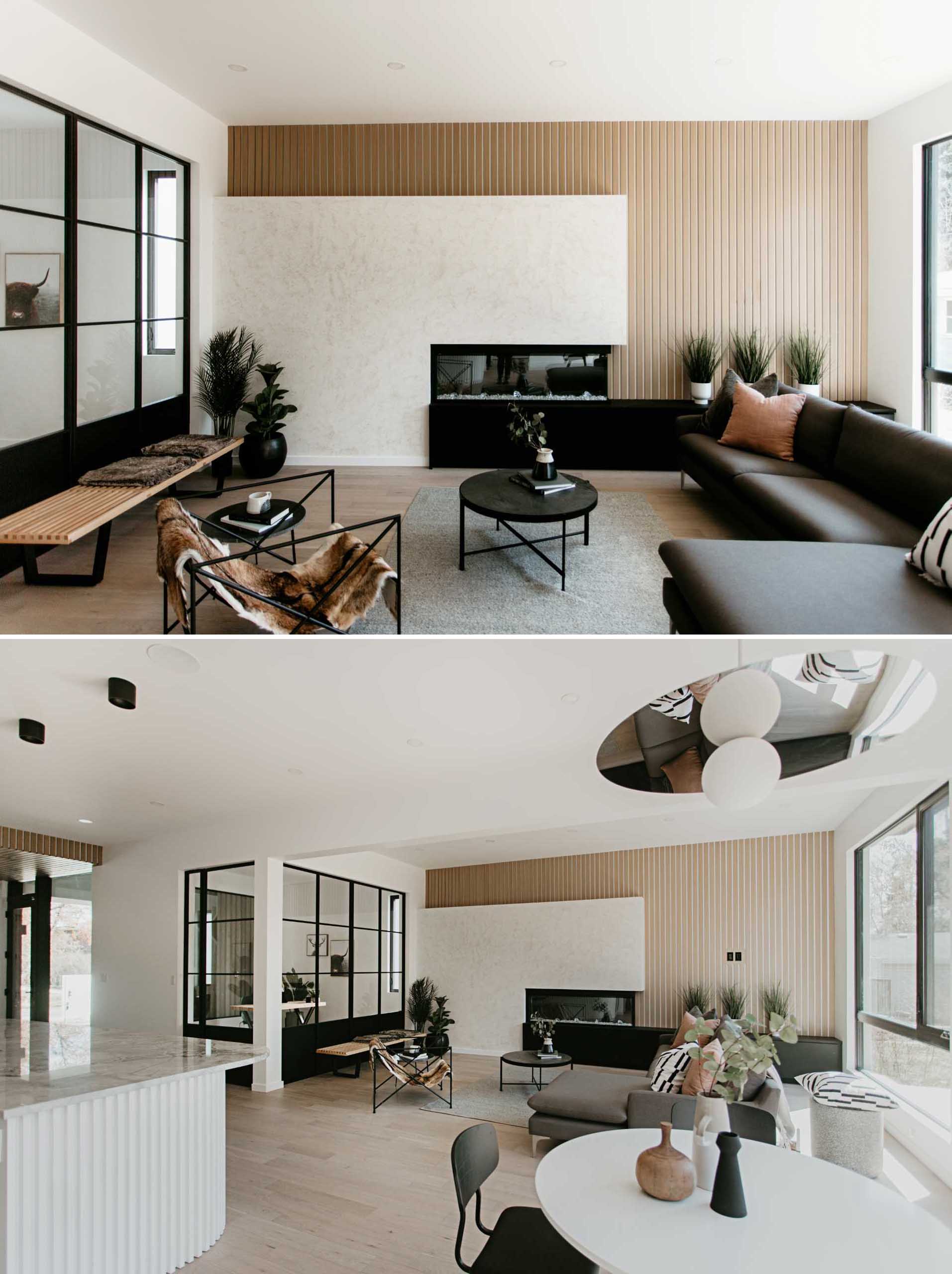 In this modern living room, there's an accent wall of wood slats, a fireplace, and black cabinets, while a section of interior windows provides a view of the home office.