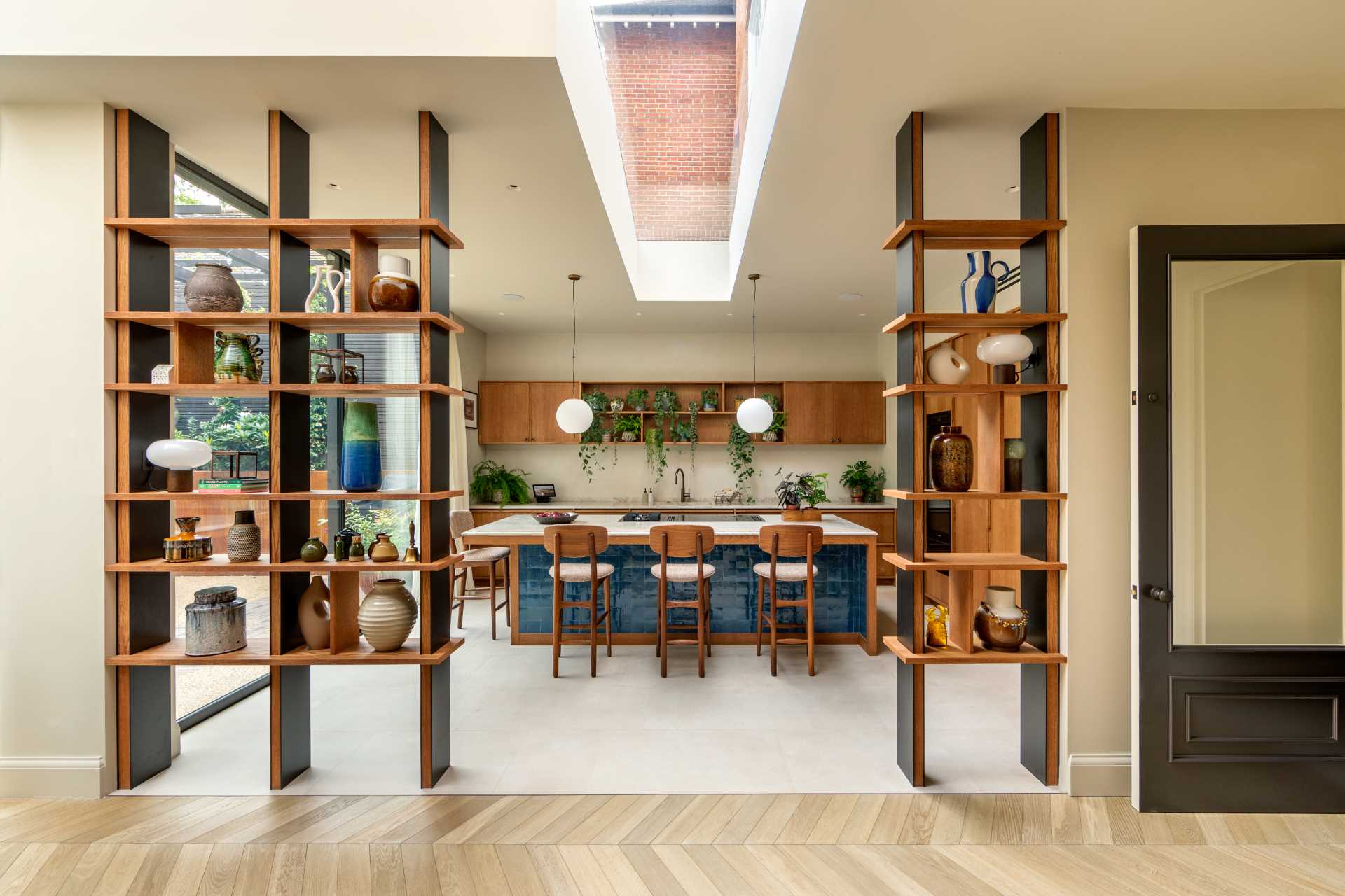 این اتاق ناهار خوری دارای منظره ای از آشپزخانه است، در حالی که قفسه های کتاب از کف تا سقف یک ورودی برای آشپزخانه ایجاد می کند.