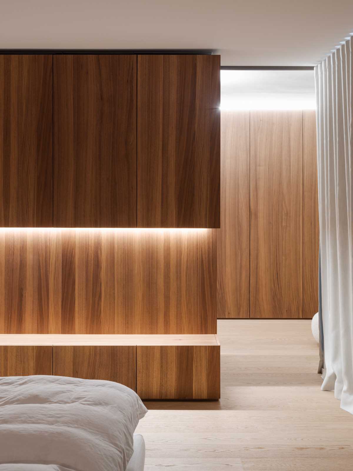 In this primary bedroom, wood cabinetry and wood floors add a sense of warmth, while hidden lighting creates a soft and relaxing glow.