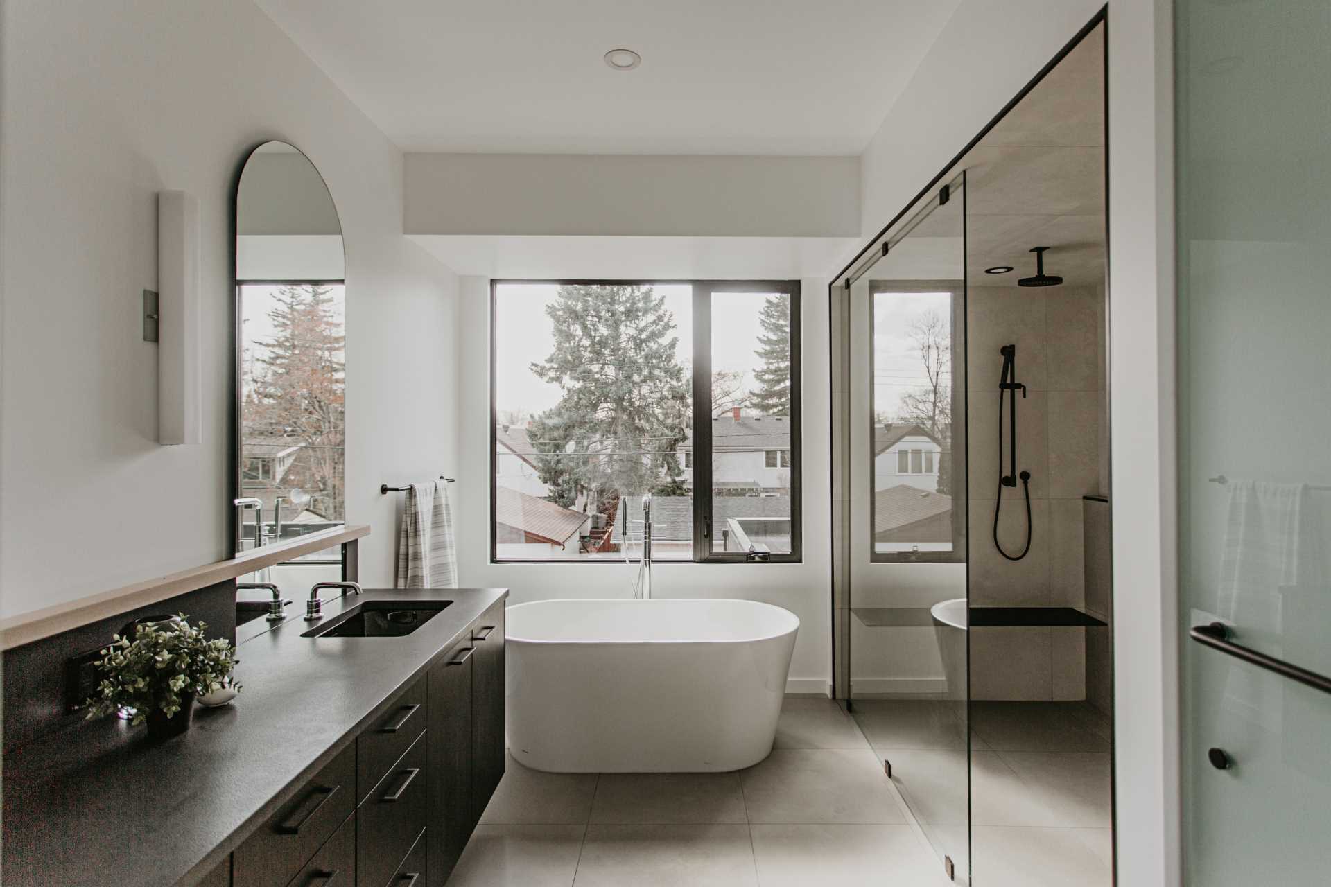 In the primary bathroom, grey and white tiles contrast with a black-on-black vanity, while curves are added with arched mirrors.