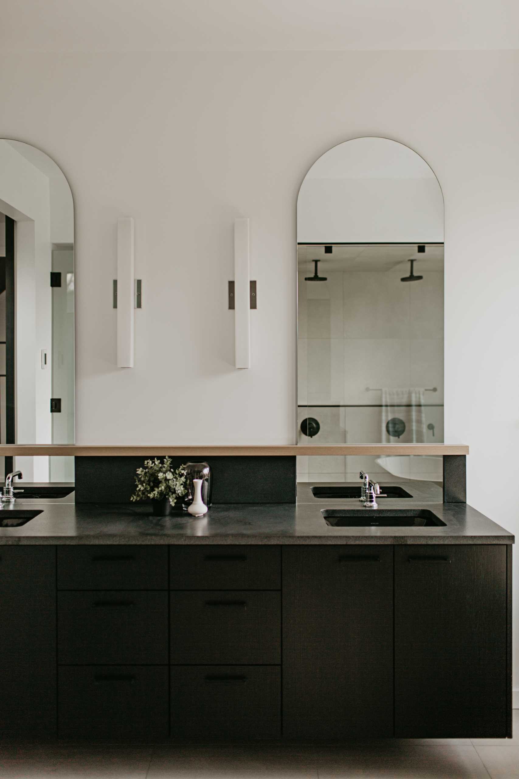 In the primary bathroom, grey and white tiles contrast with a black-on-black vanity, while curves are added with arched mirrors.