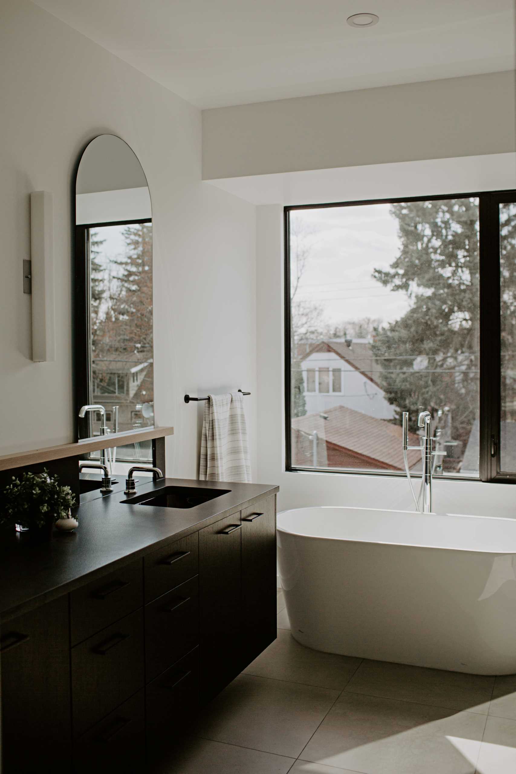 A modern primary bathroom with a freestanding bathtub below the window, and a black vanity.