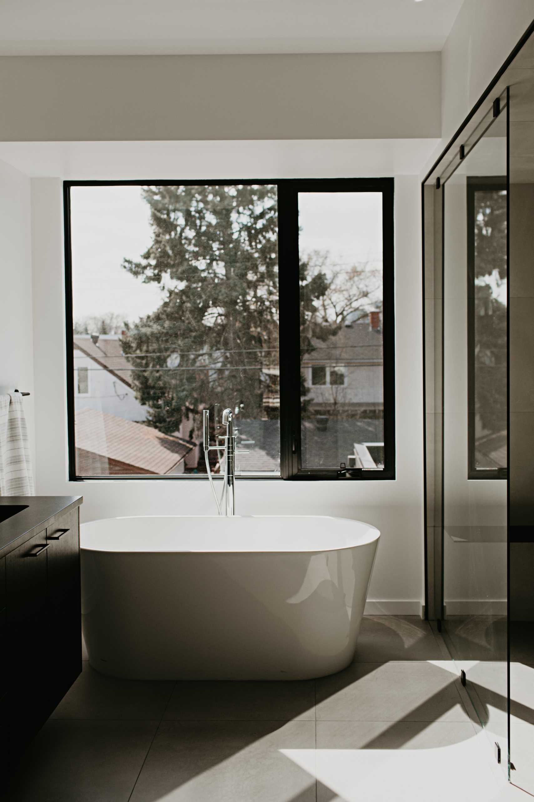 A modern primary bathroom with a freestanding bathtub below the window.