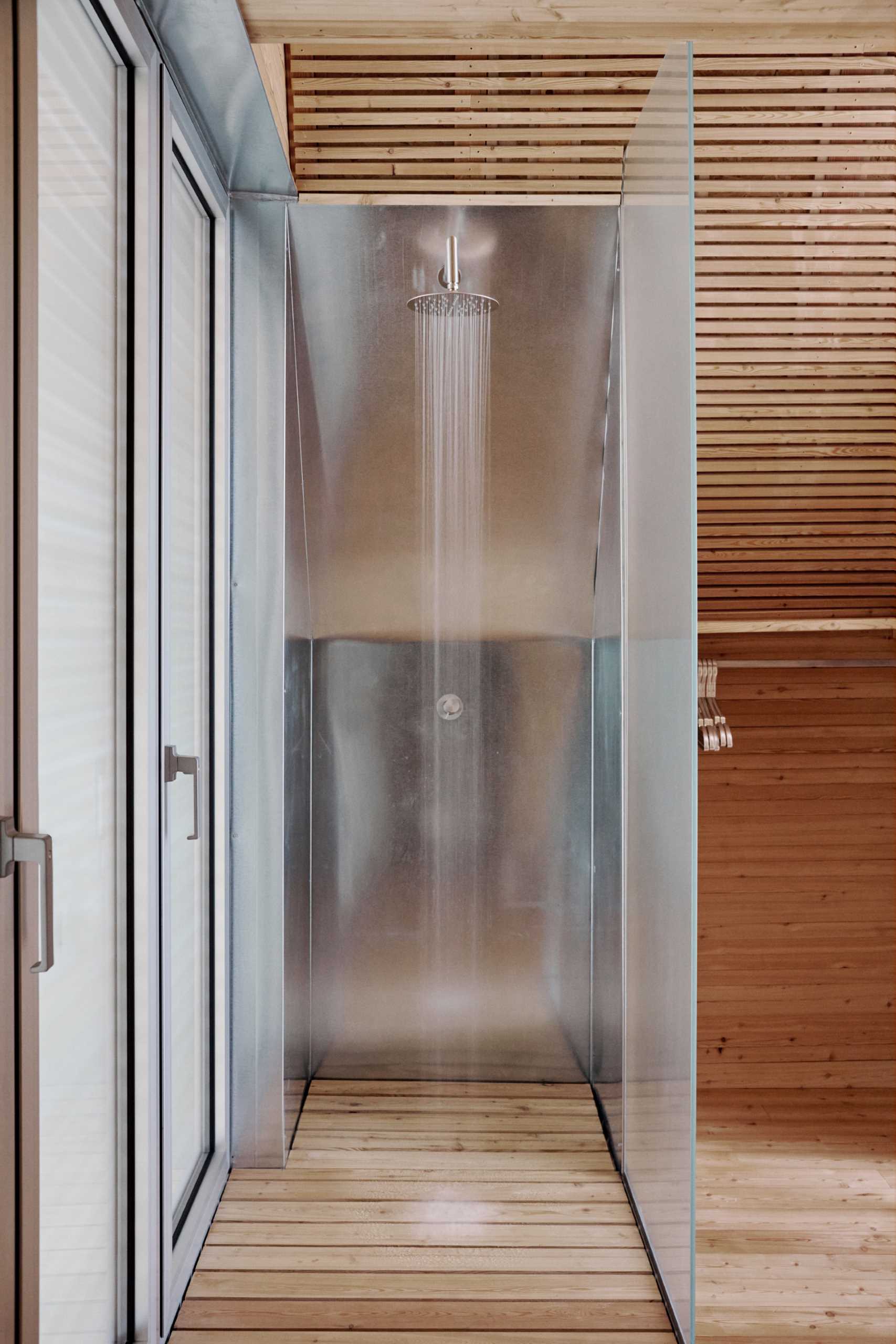 A minimalist metal and glass lined shower with a wood floor.
