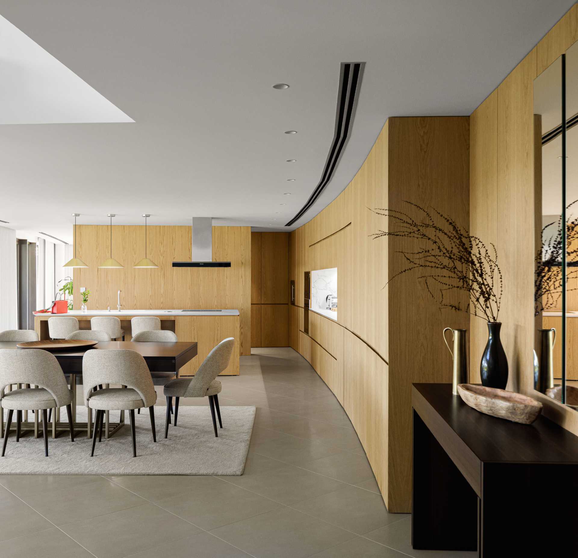 Warm wood walls and cabinets, and concrete floors connect the living room with the kitchen and dining area. The cabinetry that lines the wall also follows the curvature of the home.