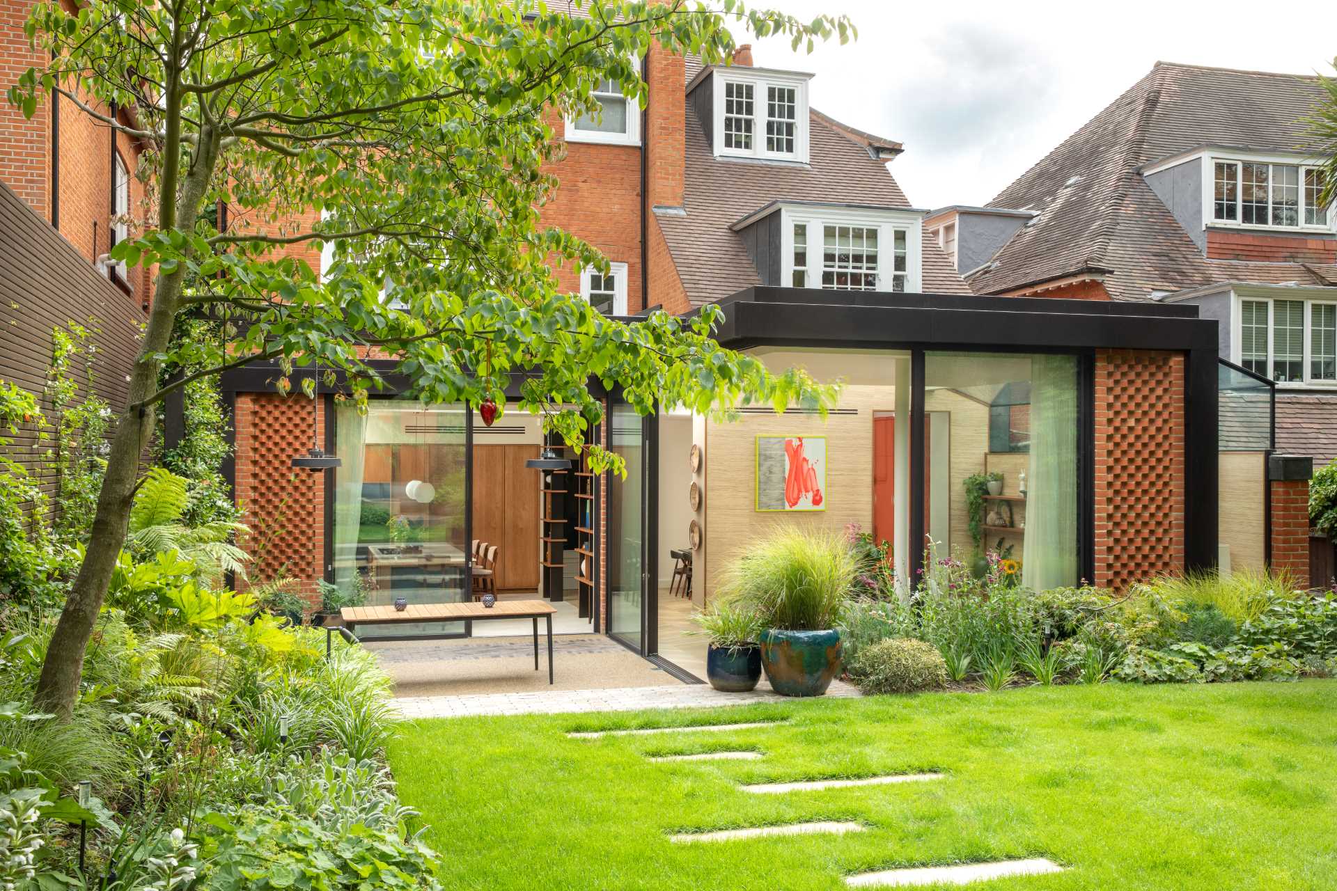 The black steel frame contrasted against the color of the red clay brick facade, while the glass sliding doors create a frame around the new living space as it leads seamlessly into the garden.