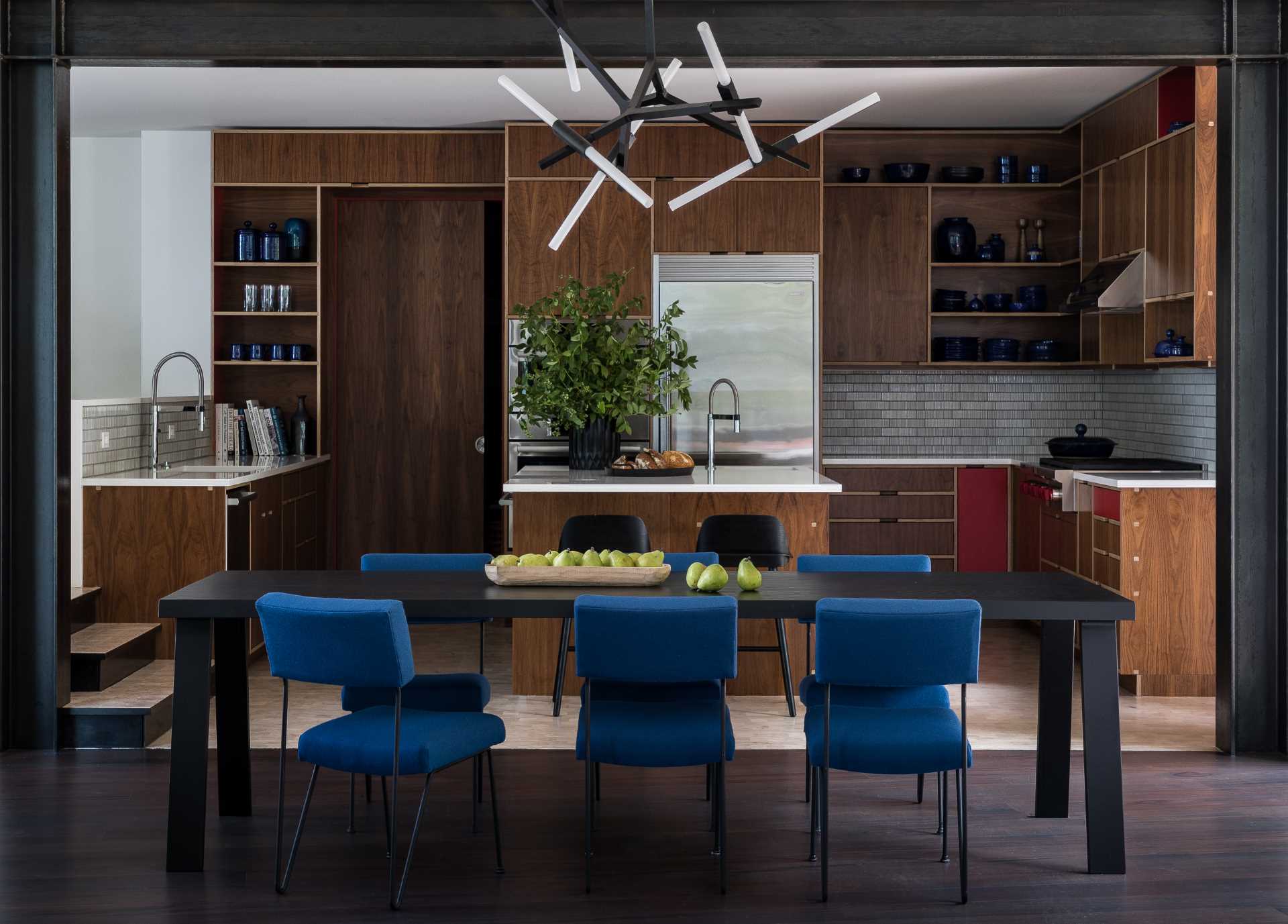 A modern open plan dining room and kitchen, with blue chairs and walnut cabinets.