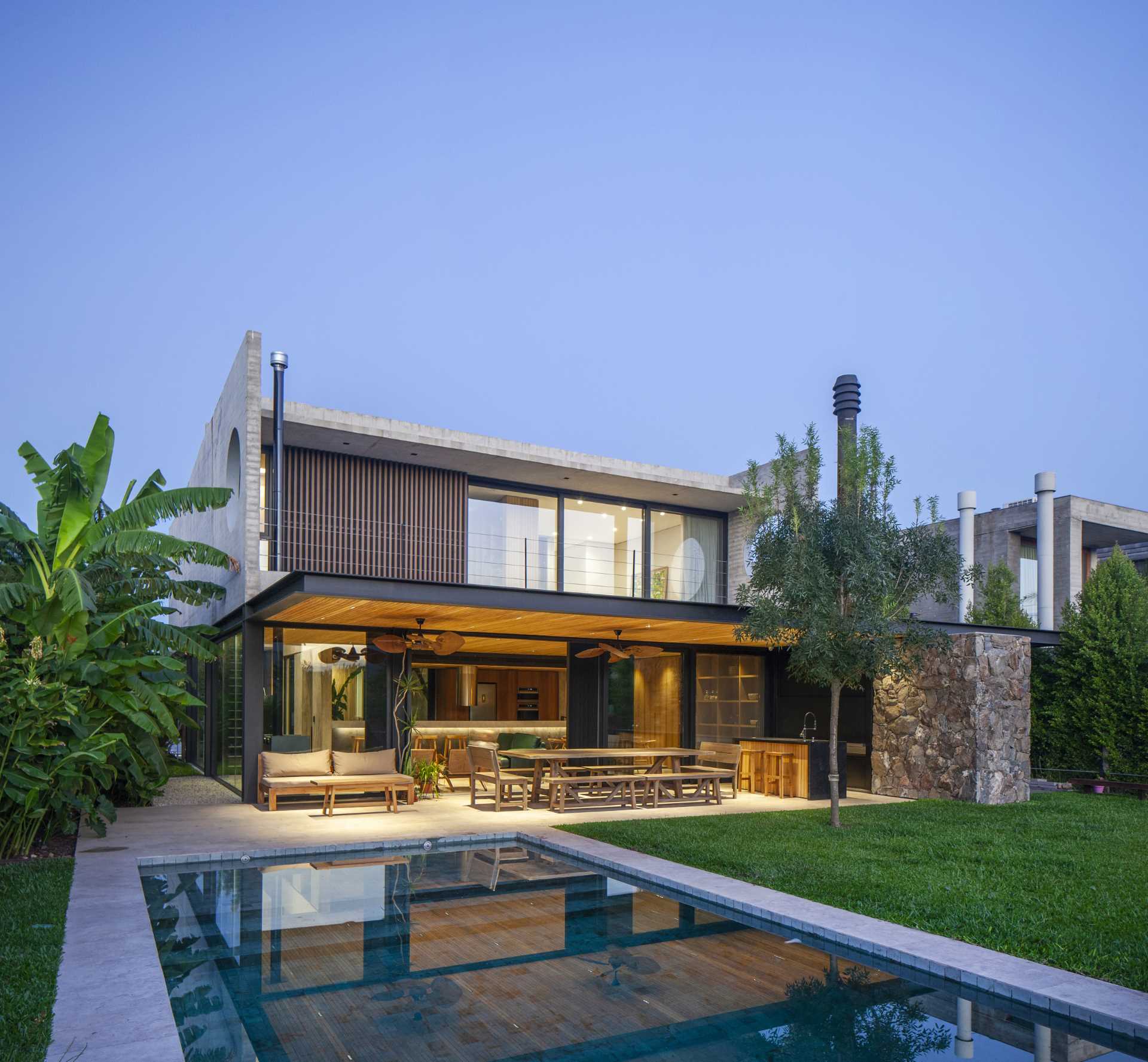 A modern stone and concrete home with a covered patio, pool, and yard.