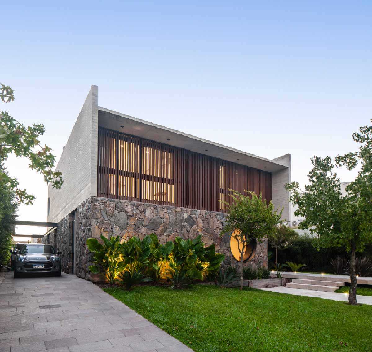 A modern home with a stone, wood, and concrete facade, that also includes a round window.