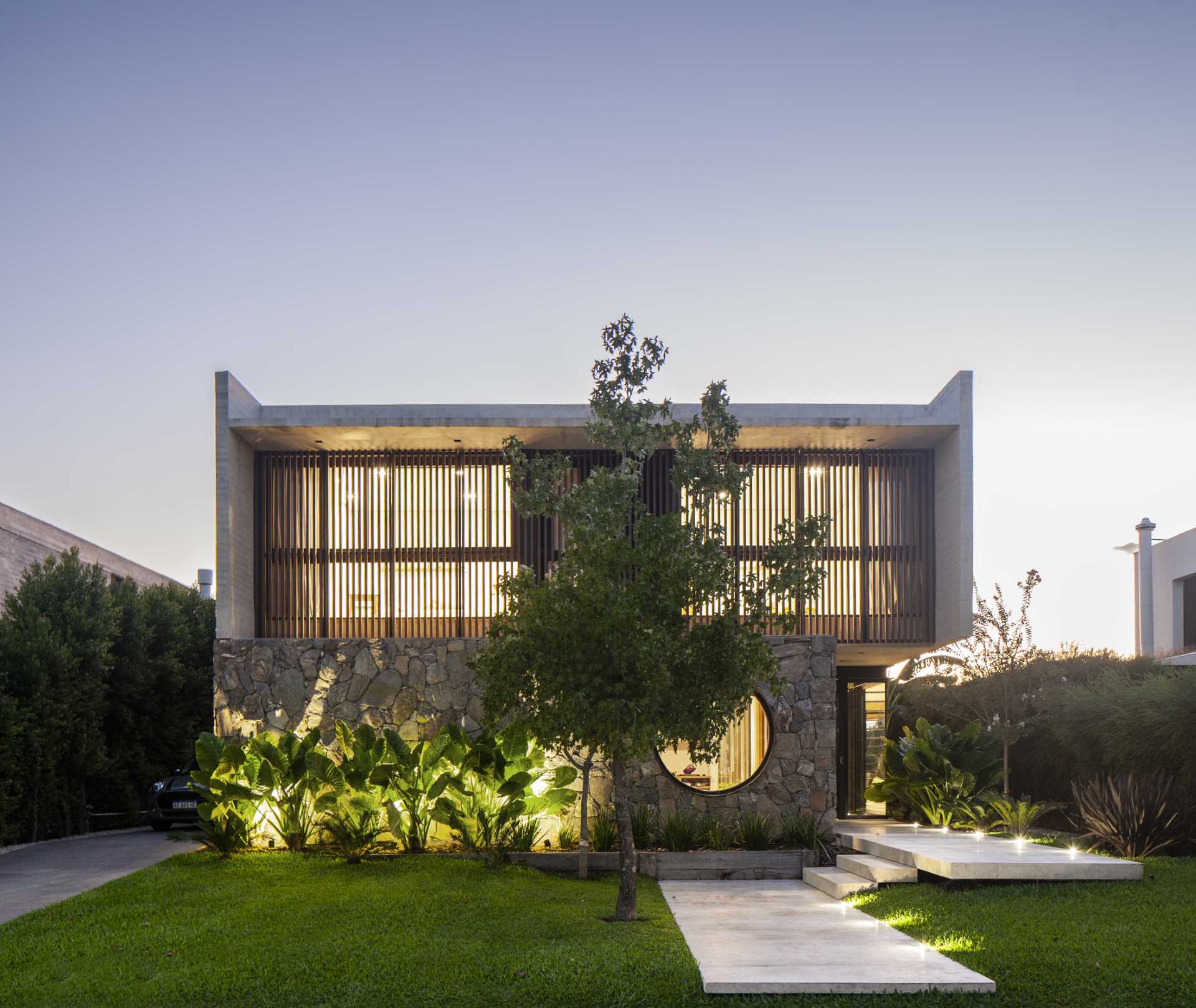 A modern home with a stone, wood, and concrete facade, that also includes a round window.