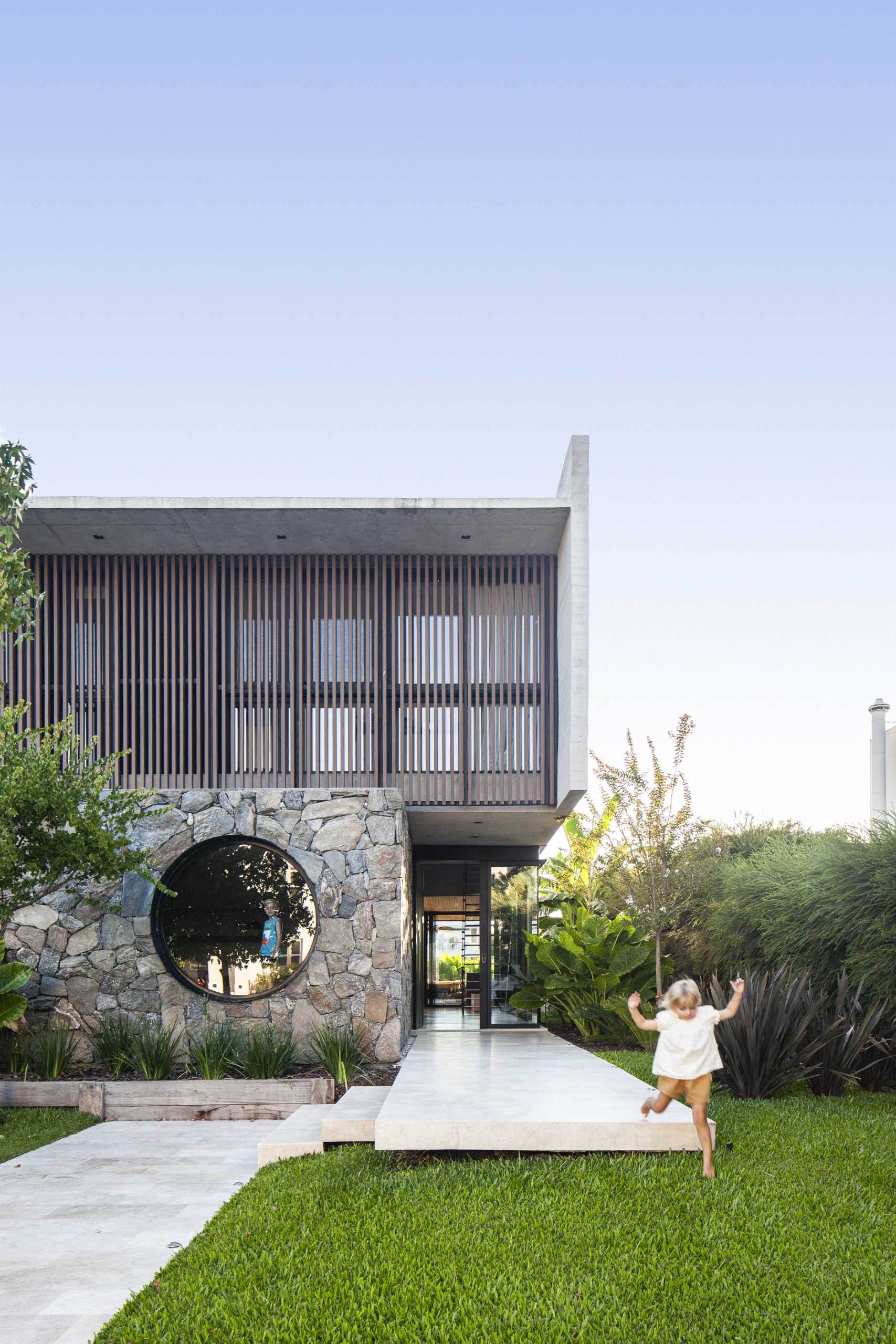 A modern home with a stone, wood, and concrete facade, that also includes a round window.