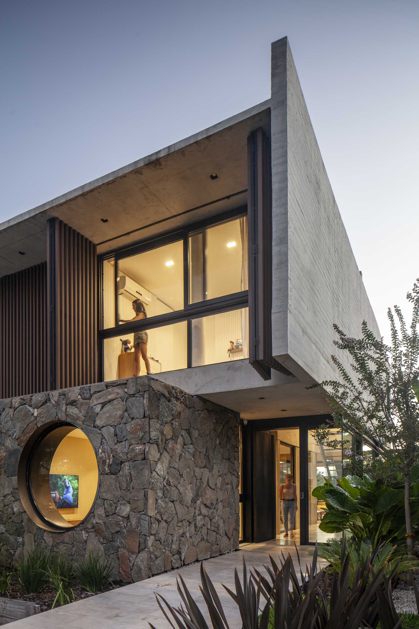 A modern home with a stone, wood, and concrete facade, that also includes a round window.