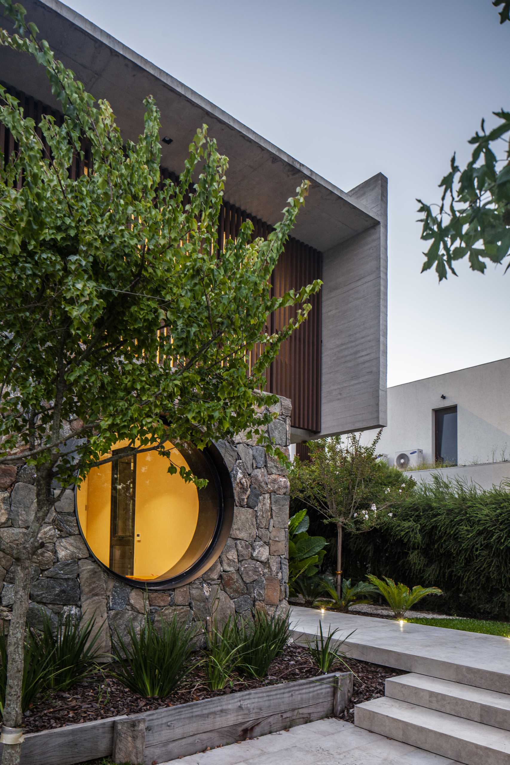 A modern home with a stone, wood, and concrete facade, that also includes a round window.