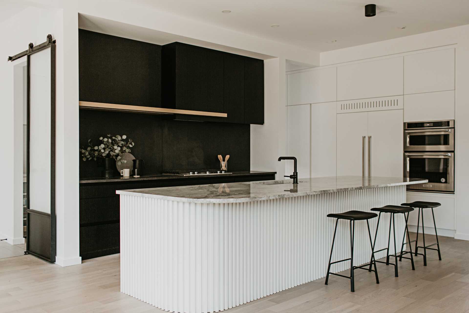 The design of this modern kitchen has a highly contrasting black and white look. To soften the starkness, a curve in the super white dolomite countertop on the island is replicated onto a base with painted wood slats.